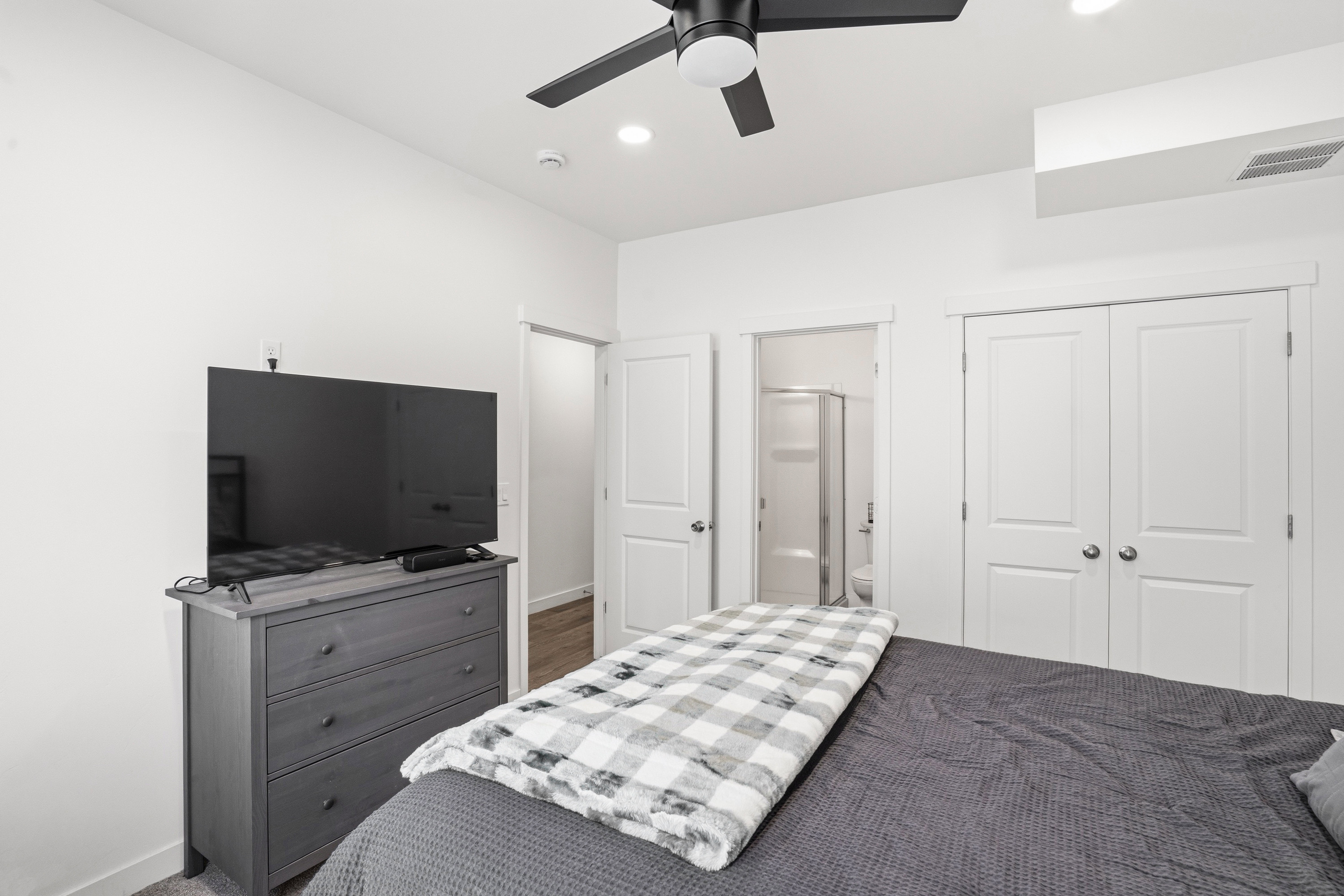 White painted walls and trim throughout, featuring a black ceiling fan with integrated lighting, recessed ceiling lighting, and a double-door closet with chrome hardware