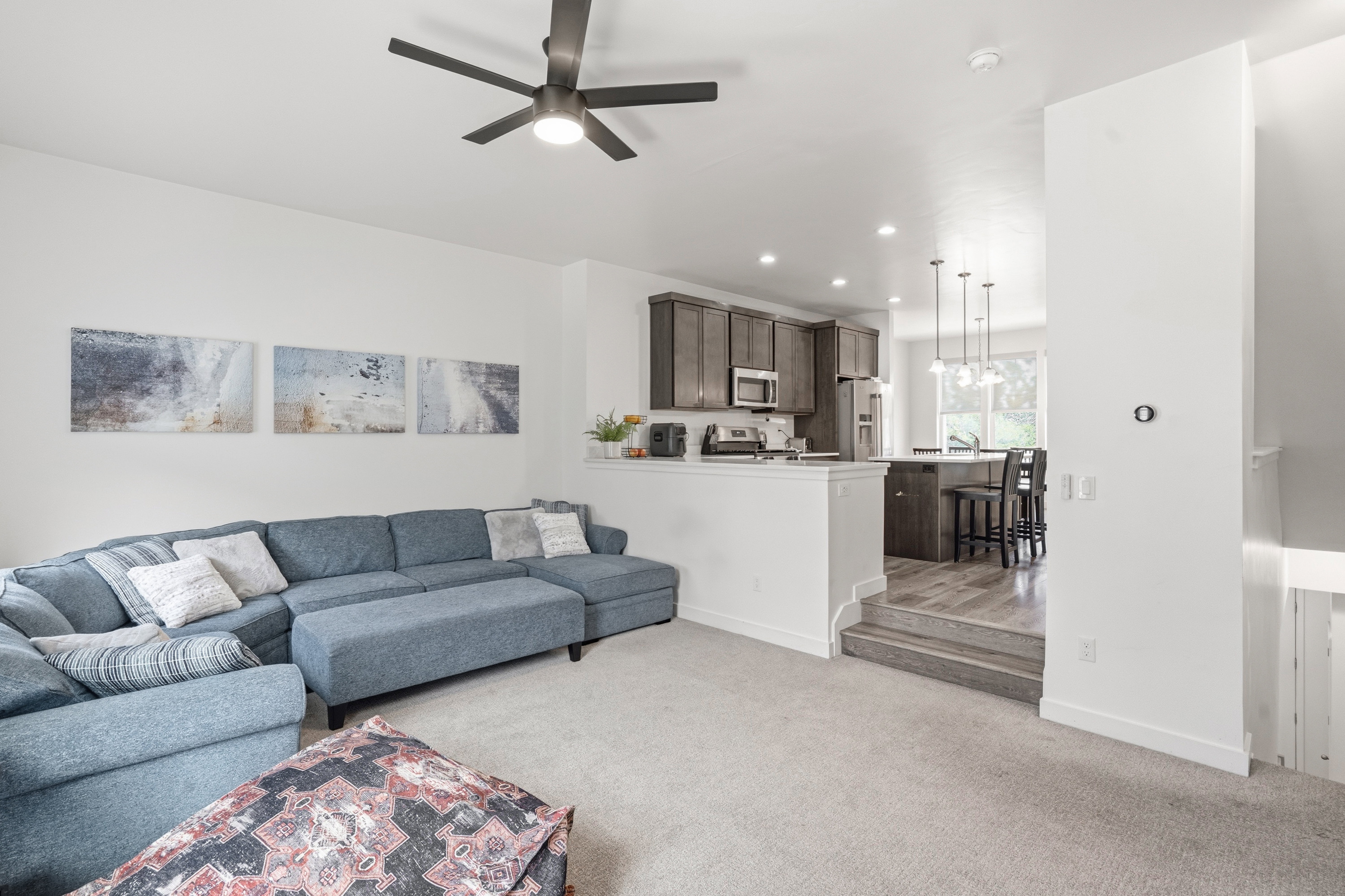 Open-concept living area with light-colored carpeting, a dark-toned ceiling fan, and recessed lighting