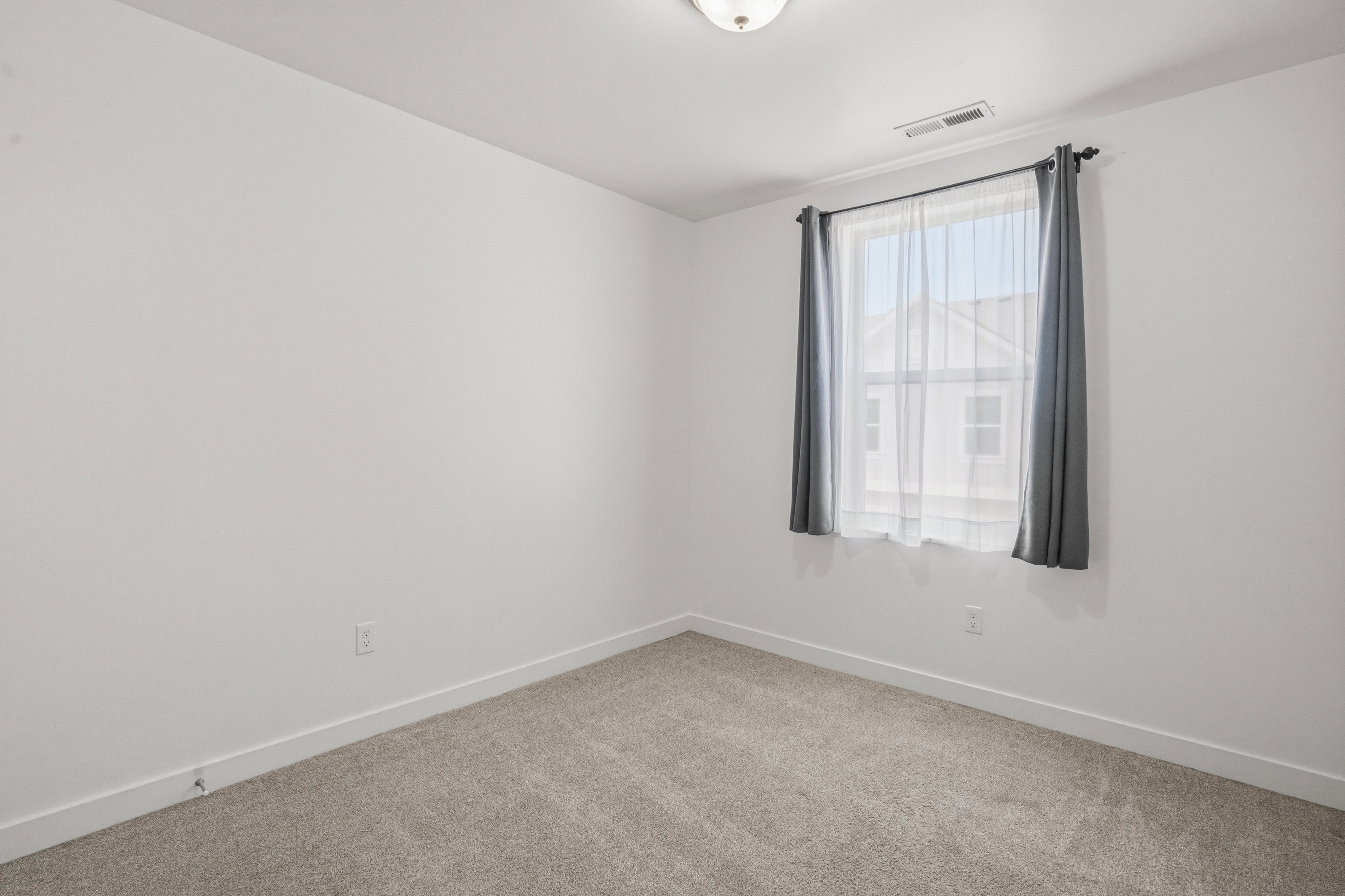 Carpeted room featuring a single window with curtain rod and drapes, white walls, and a ceiling-mounted light fixture