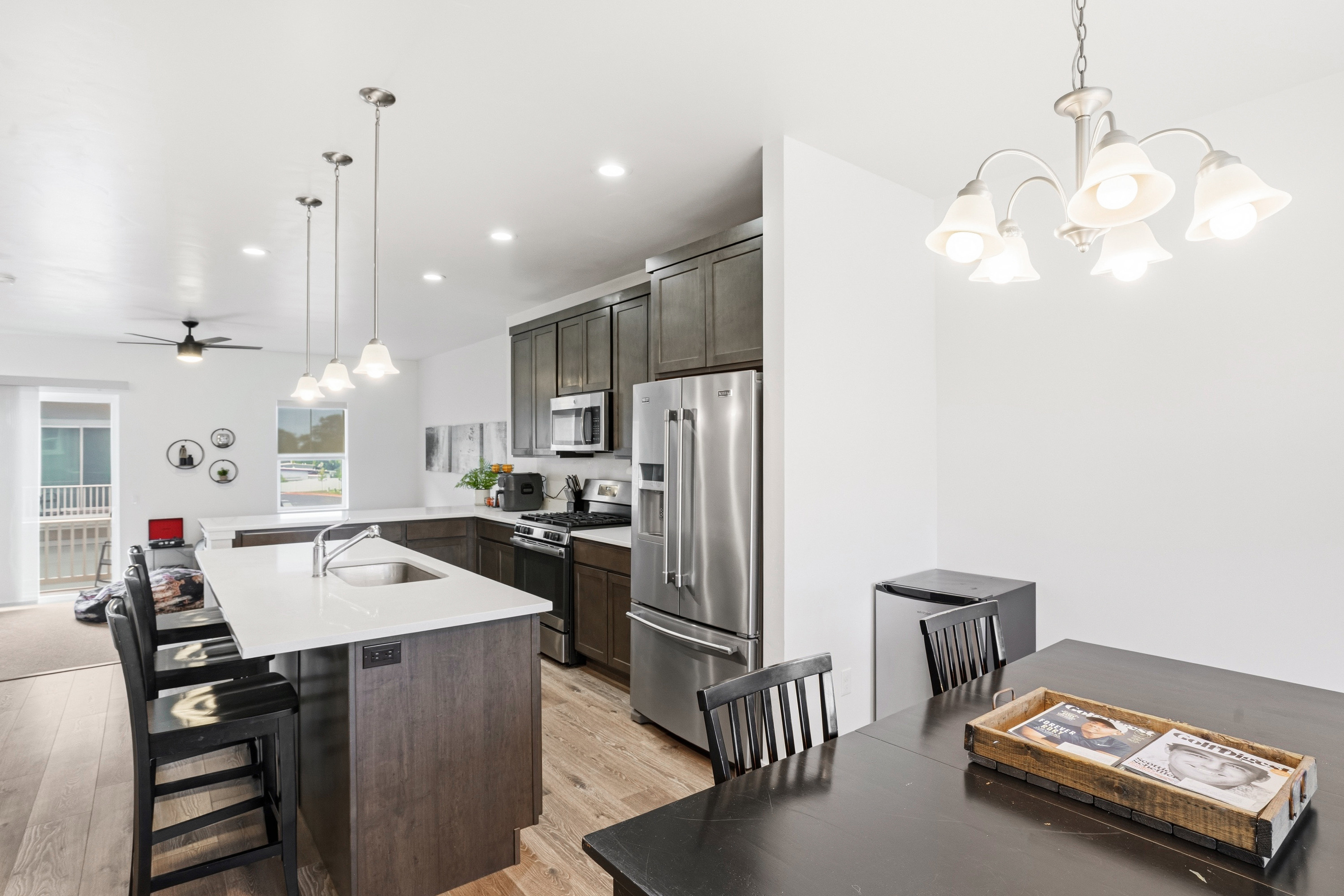 Modern kitchen featuring stainless steel appliances, dark wood-finish cabinetry, a large center island with a sink, pendant lighting, and wood-finish flooring