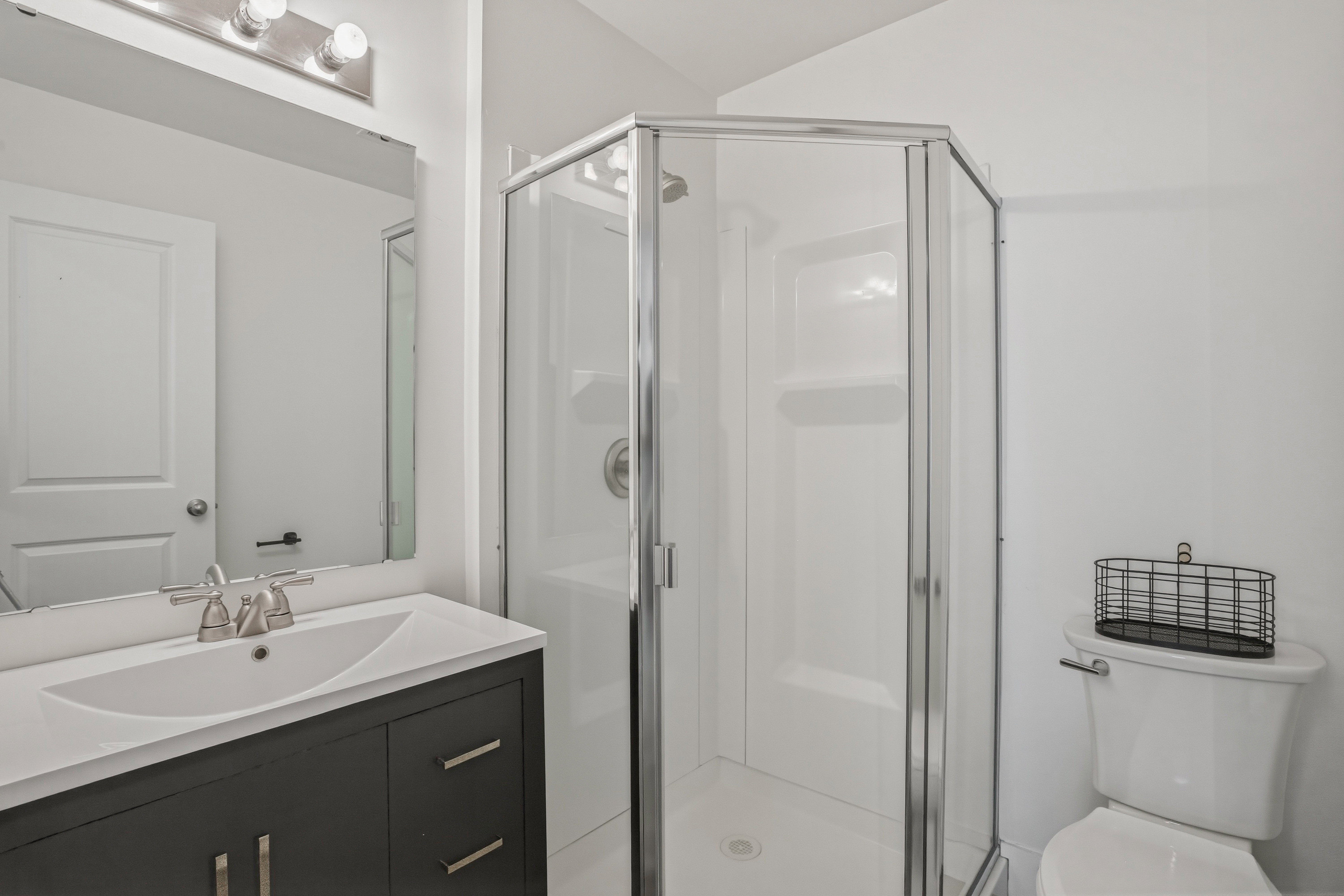 Bathroom featuring a glass-enclosed shower, dark wood-finish vanity with a white countertop, undermount sink, and brushed nickel fixtures