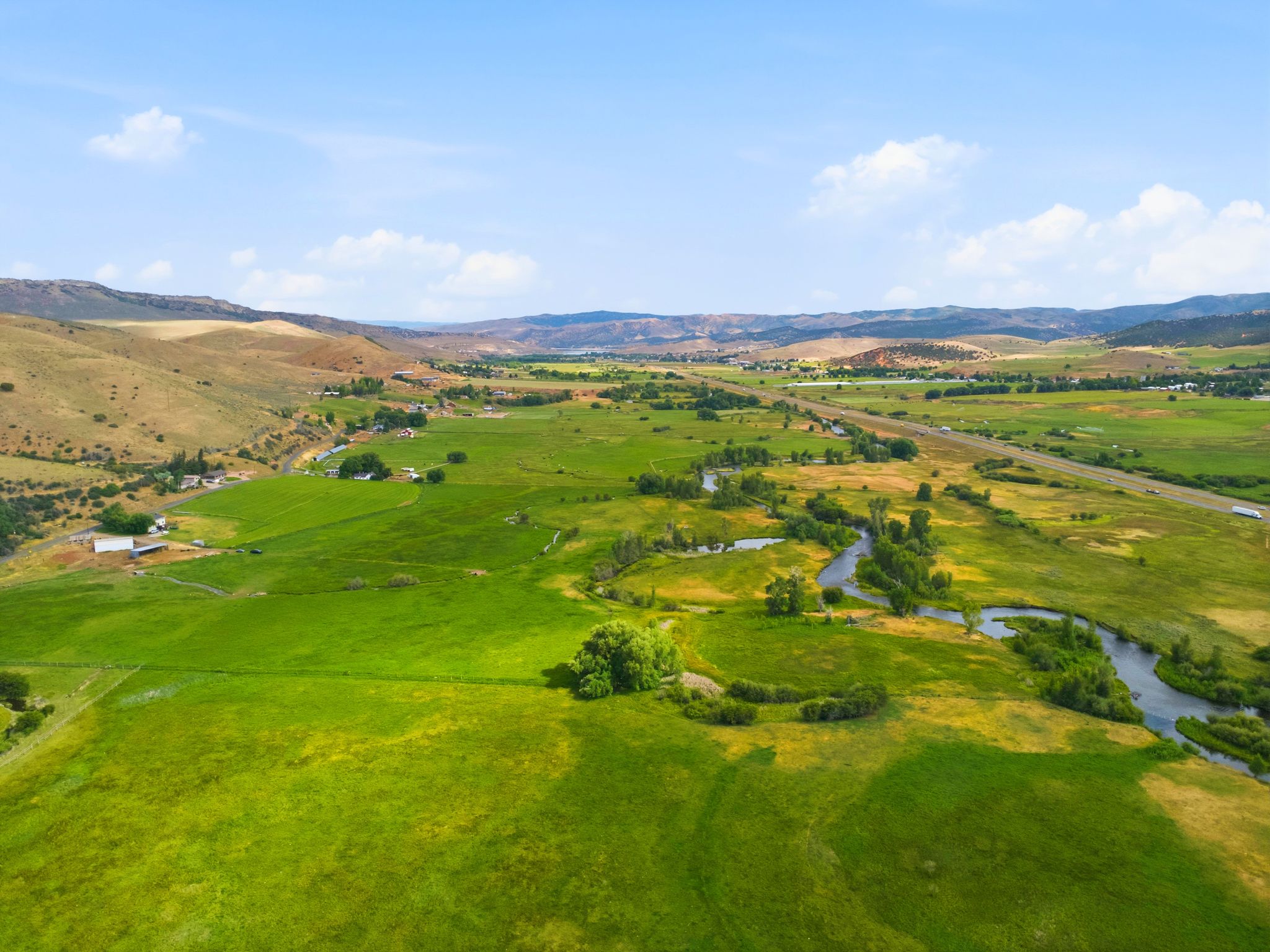 Expansive green landscape featuring a winding river, distant hills, and a prominent highway