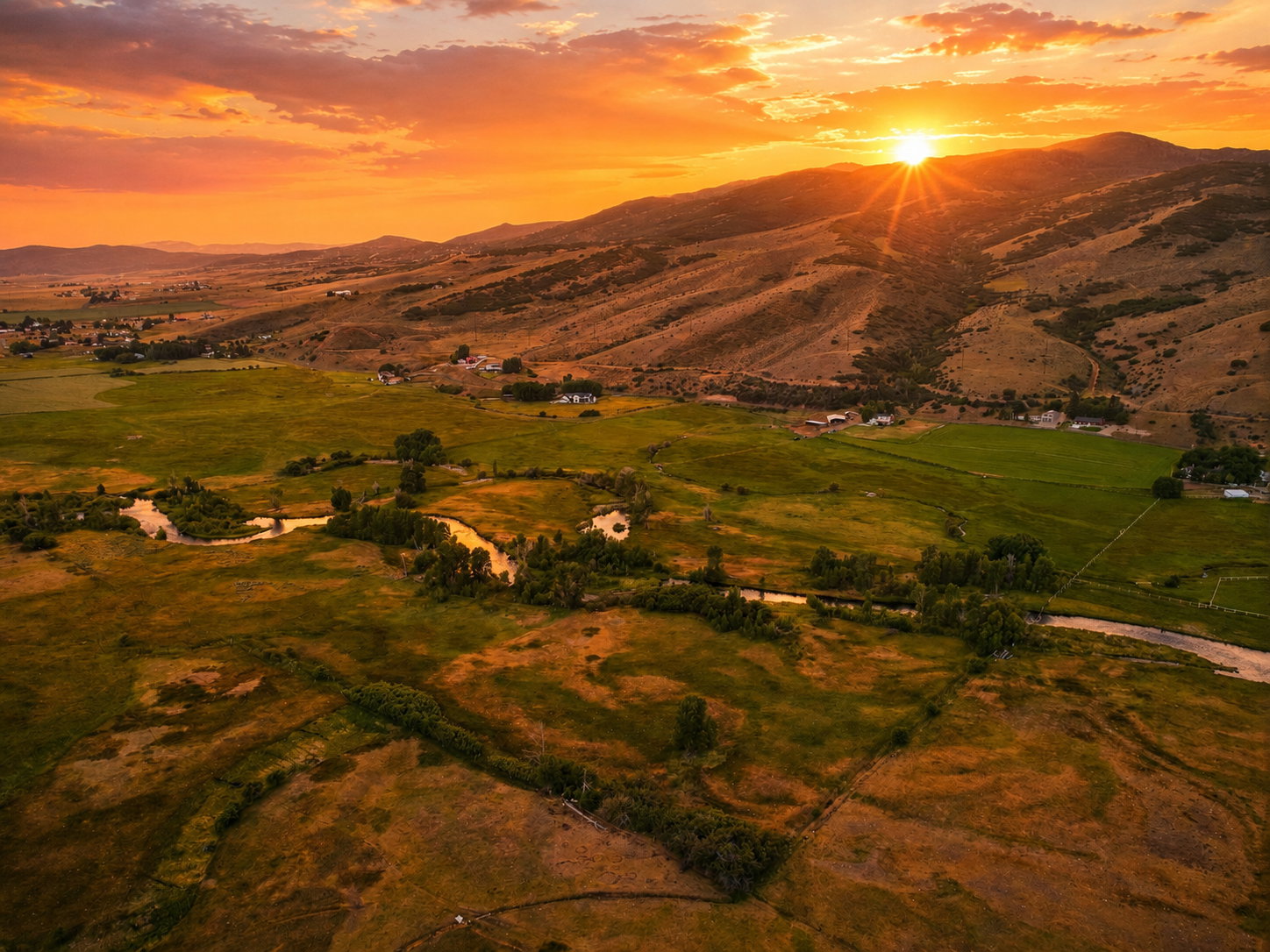 Expansive mountain landscape featuring a river, rolling hills, and scattered residential structures