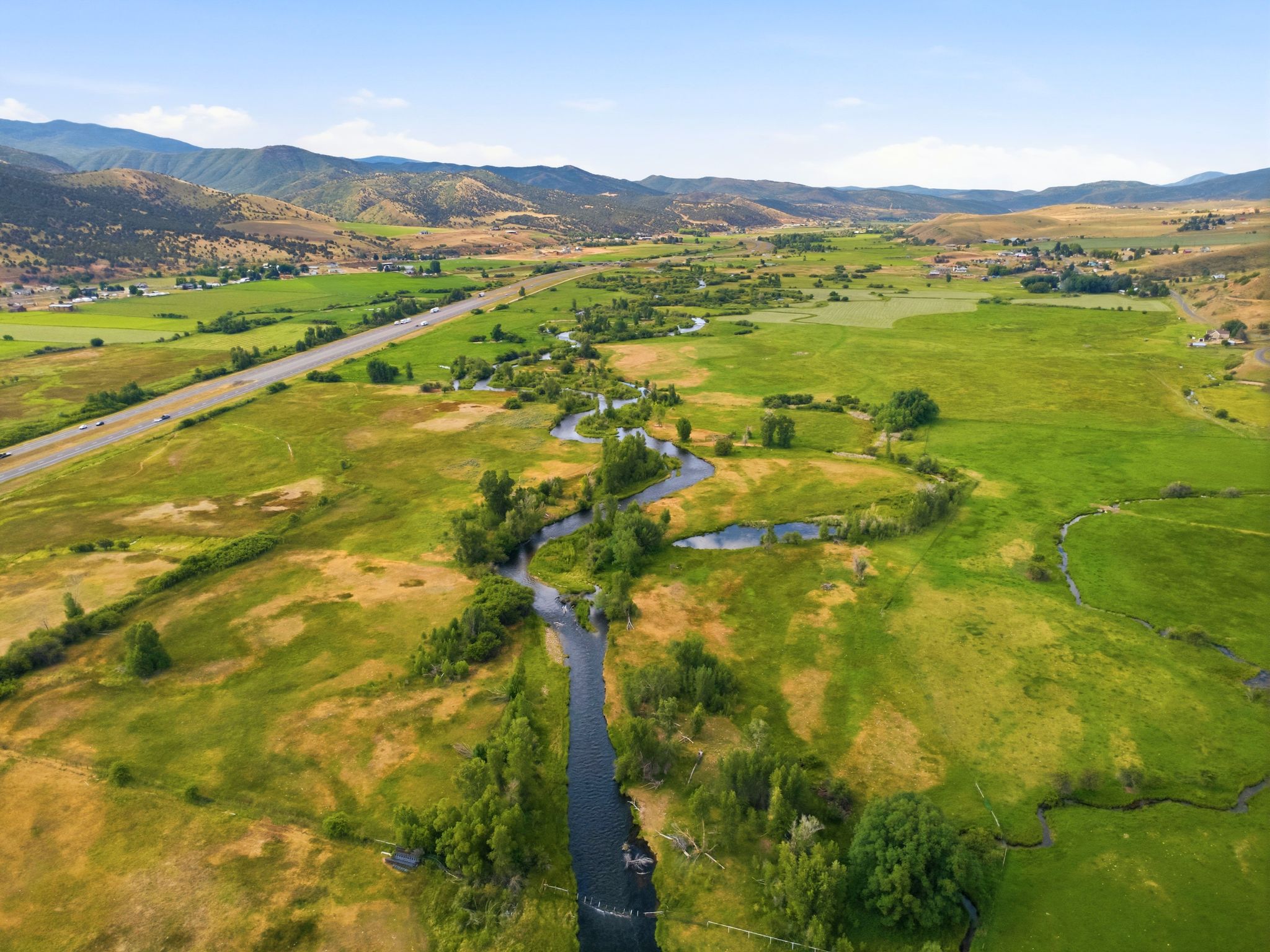 Expansive property featuring a winding river, lush green fields, and distant mountain ranges