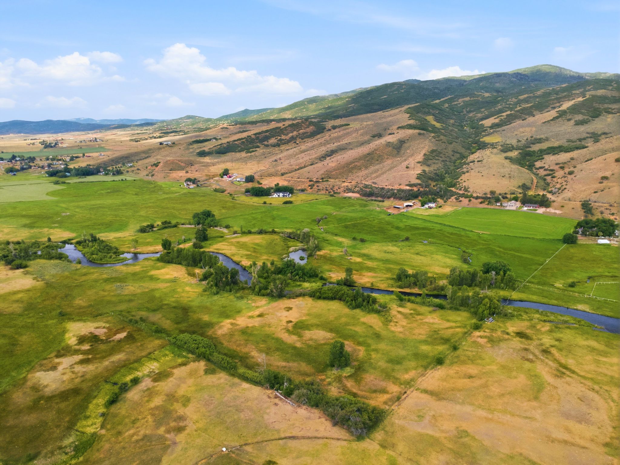 Expansive rural landscape featuring a winding river, verdant fields, and distant mountainous terrain