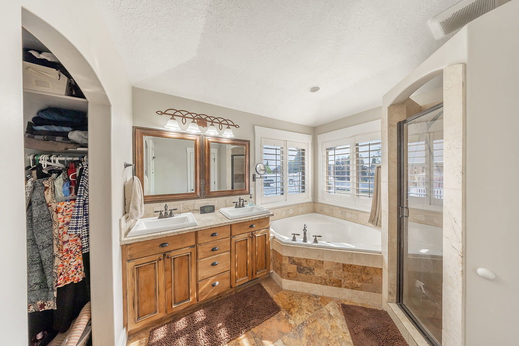 Bathroom featuring a corner soaking tub, a separate glass-enclosed shower, a dual vanity with wood cabinetry, and plantation shutters