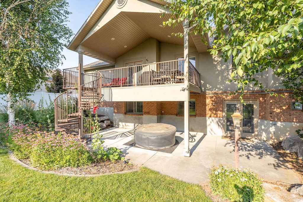 Rear exterior featuring a large upper-level deck with metal railings and a spiral staircase to the ground-level patio