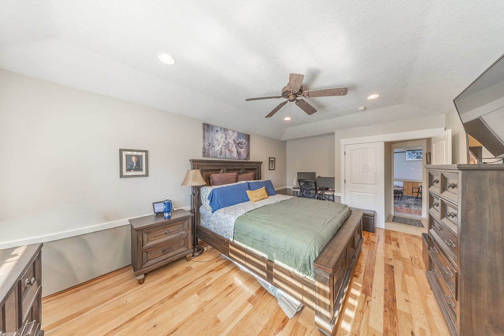 Spacious bedroom featuring wood-finish flooring, a tray ceiling with recessed lighting, and a ceiling fan