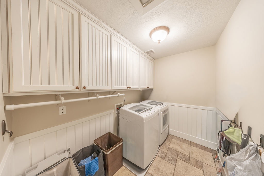 Laundry area featuring beadboard wainscoting, upper cabinetry with wood-finish knobs, and neutral-toned tile flooring