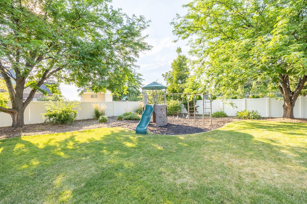Expansive backyard featuring a lush lawn, mature trees providing natural shade, and a white privacy fence