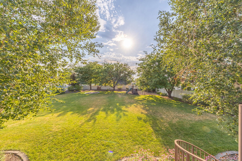 Expansive backyard featuring a large grassy lawn, mature trees, and perimeter fencing