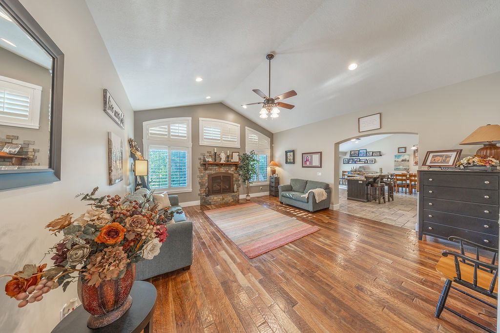 Spacious living area featuring high vaulted ceilings, rich wood-finish flooring, and a stone-faced fireplace