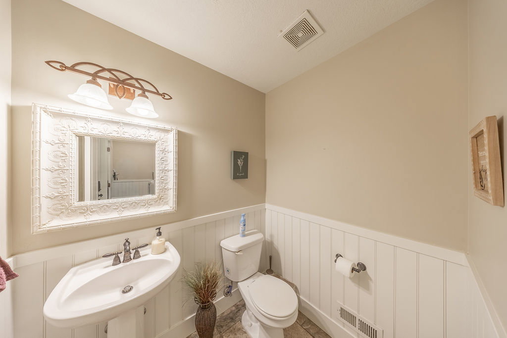 Pedestal sink with polished chrome fixtures, framed mirror with ornate detailing, and a two-light vanity fixture