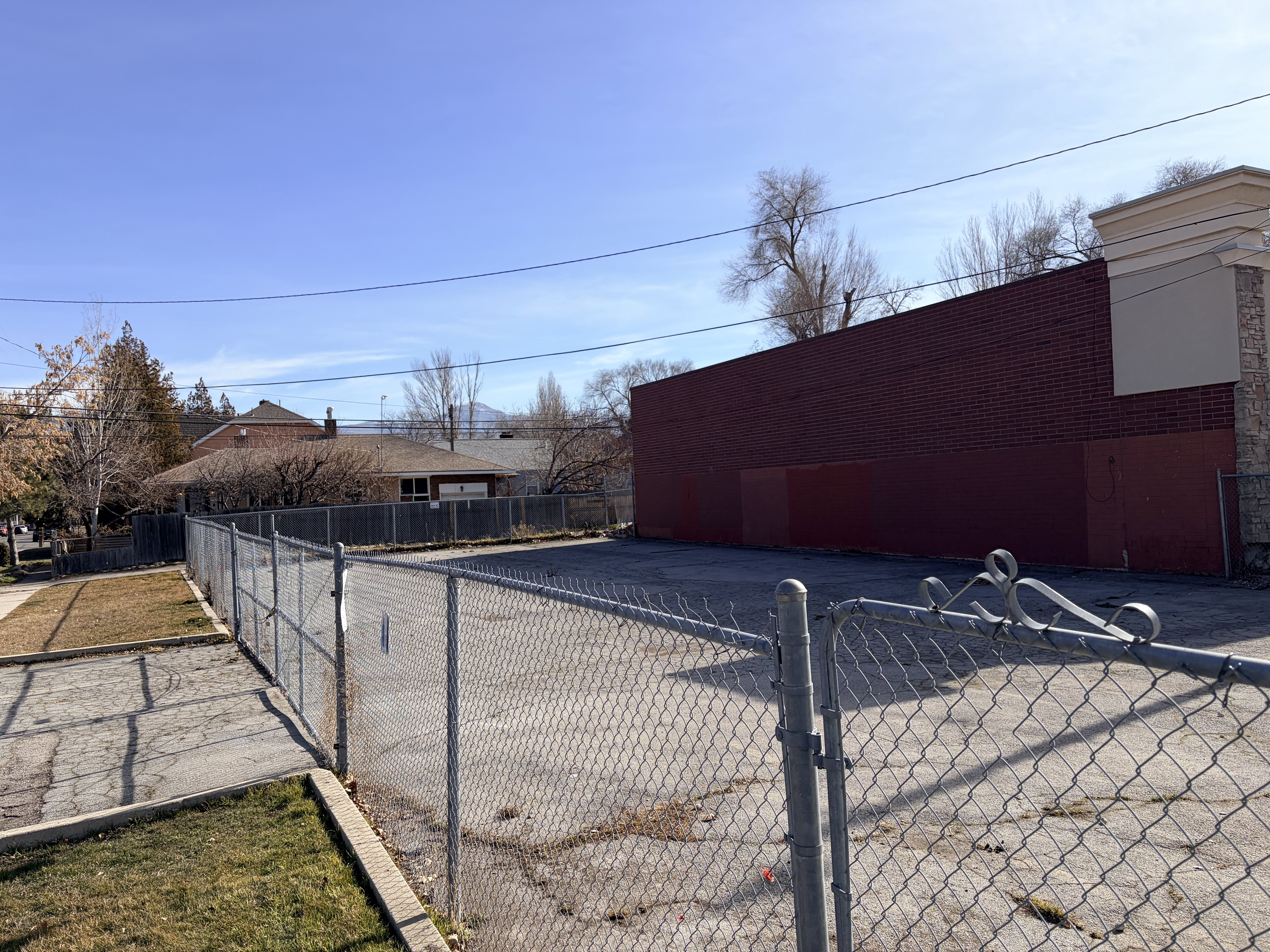 Paved lot with chain link fencing and a red brick building facade