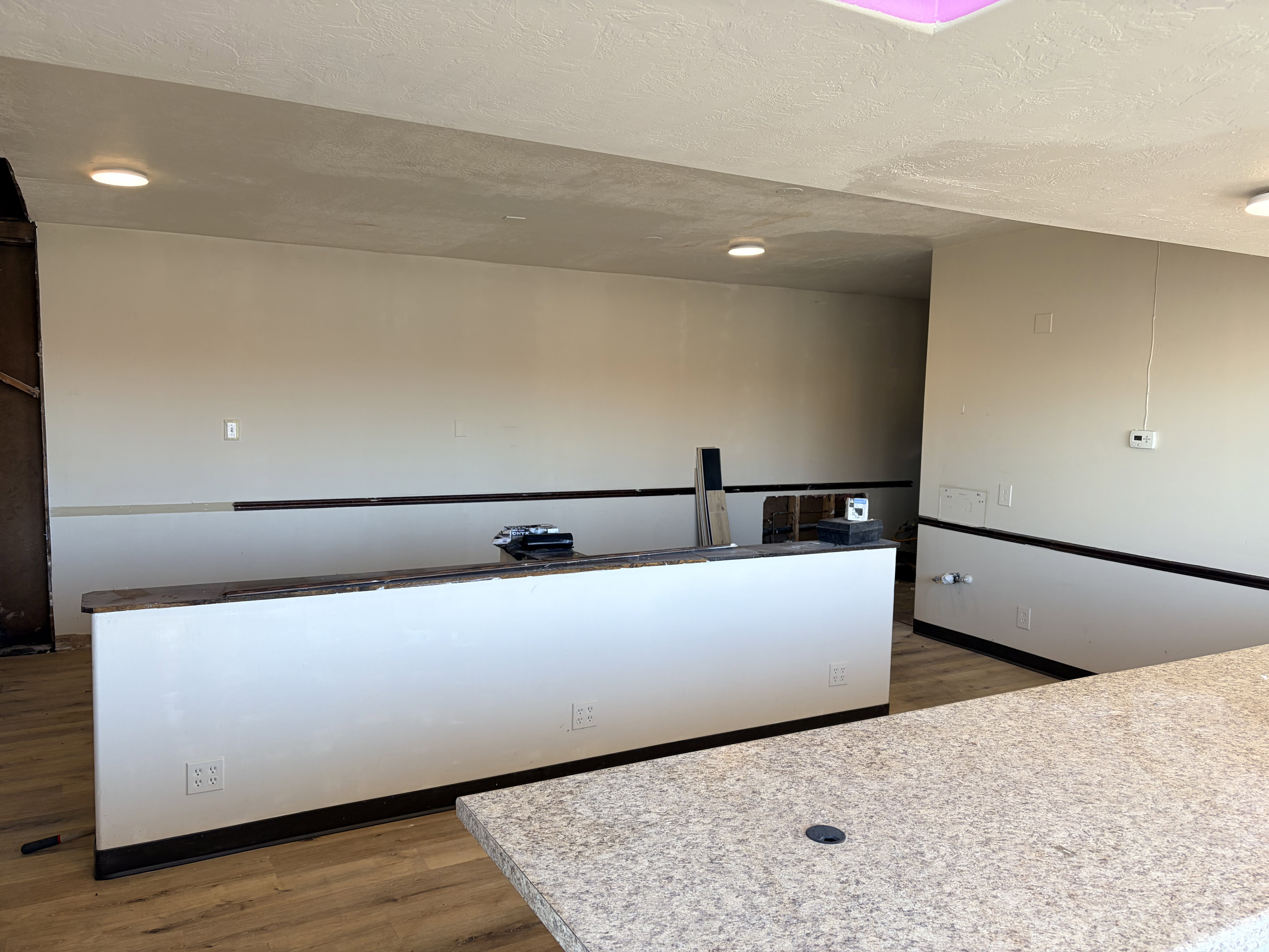 Open interior space featuring light wood-finish flooring, recessed ceiling lighting, and a built-in counter with a speckled surface