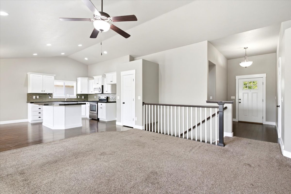 Open-concept living space featuring a kitchen with white cabinetry, dark countertops, and stainless steel appliances