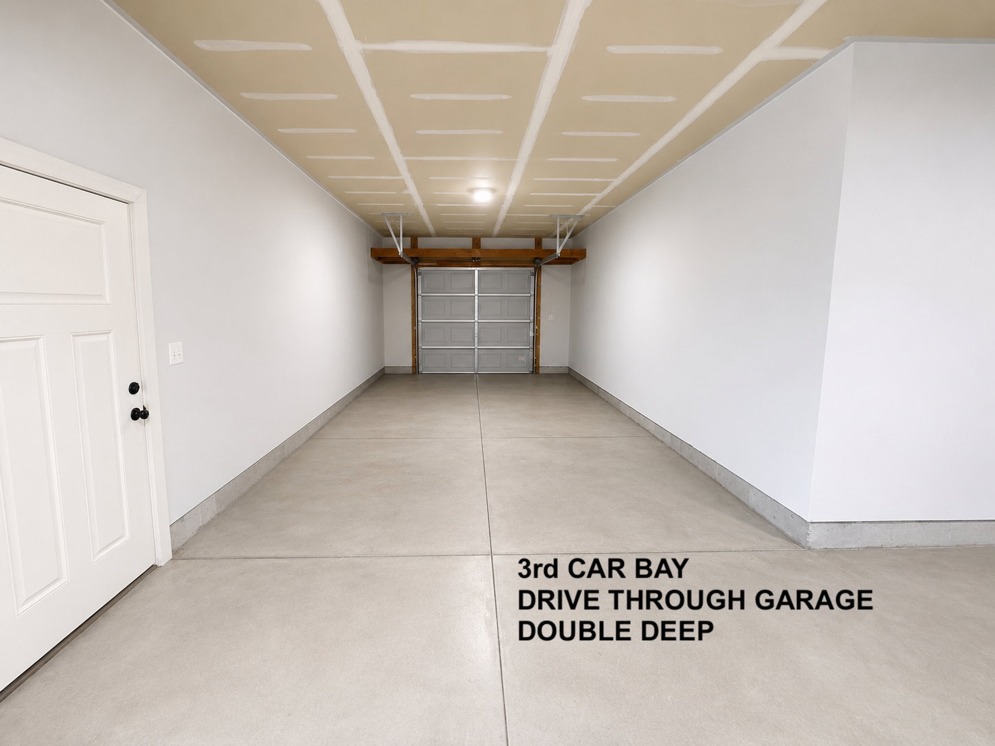 Spacious garage featuring a concrete floor, white painted walls, exposed ceiling joists, and a sectional garage door