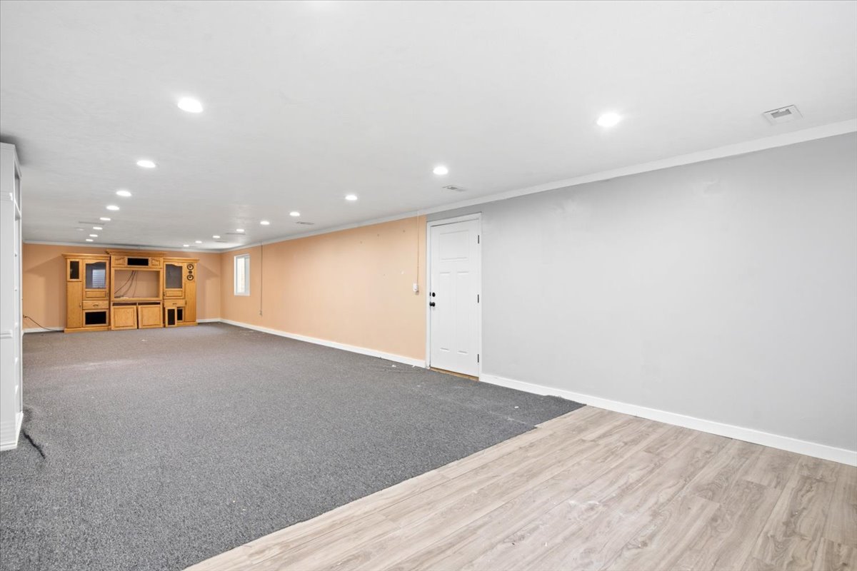 Spacious room featuring recessed lighting, a built-in entertainment center, a white paneled door, and a combination of carpet and wood-finish flooring