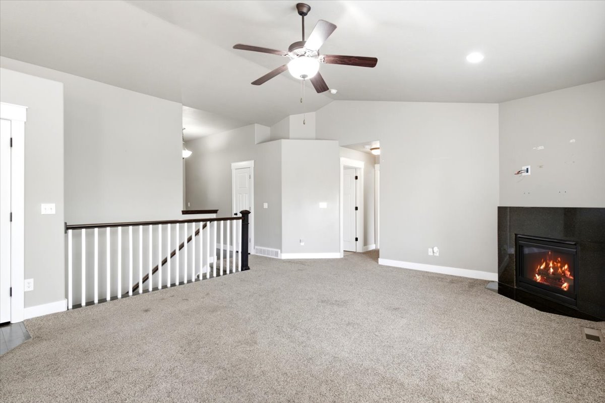 Spacious interior room featuring a corner fireplace with a dark surround, vaulted ceiling, and a ceiling fan with integrated lighting