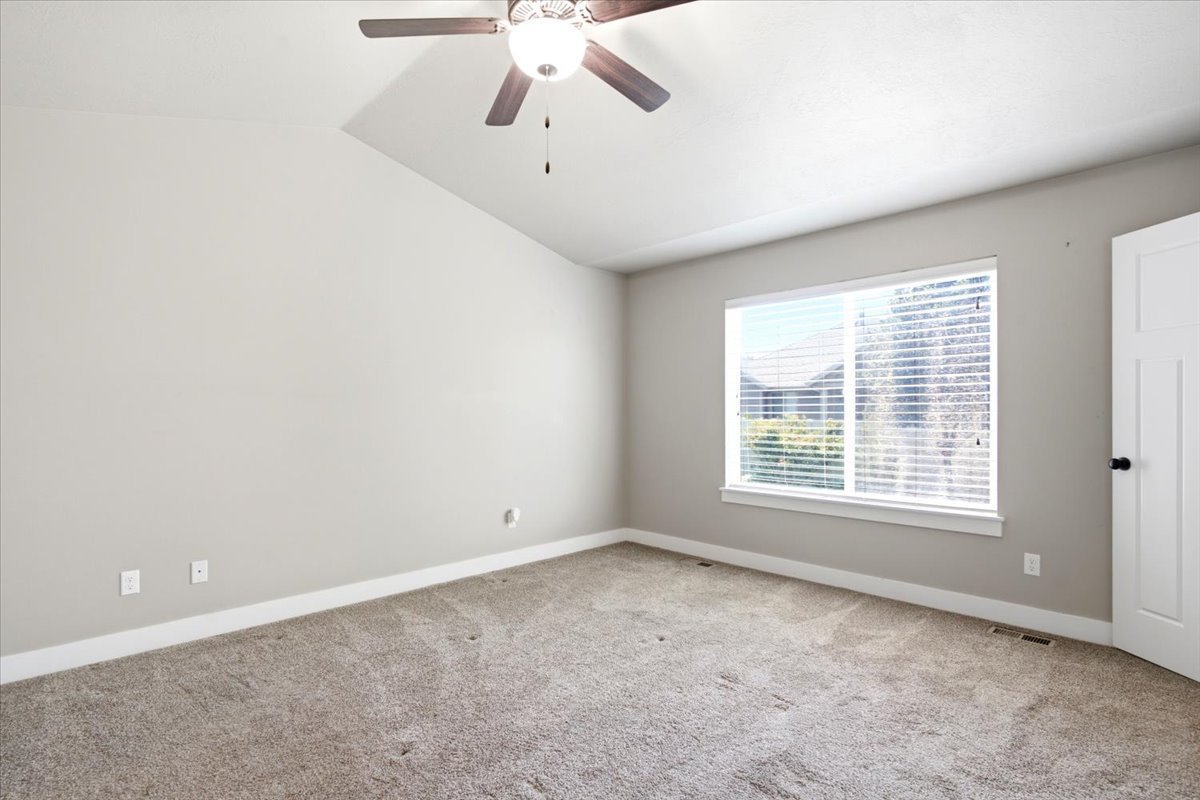 Interior room featuring a vaulted ceiling with a ceiling fan, a large window with horizontal blinds, neutral wall paint, and carpet flooring