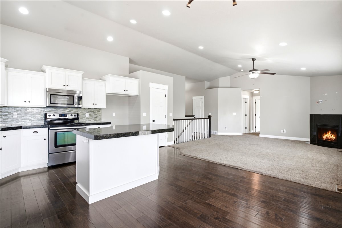 Open-concept living space featuring a kitchen with white cabinetry and dark countertops, stainless steel appliances, a tile backsplash, and a central island
