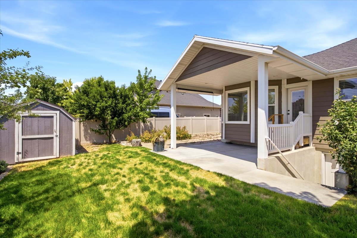 Expansive backyard featuring a covered patio, concrete walkway, and a detached storage shed