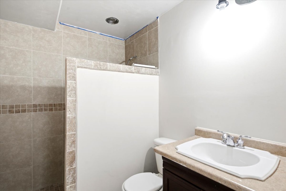 Bathroom featuring a walk-in shower with tile surround and decorative accent band, a built-in vanity with a countertop sink, and overhead lighting