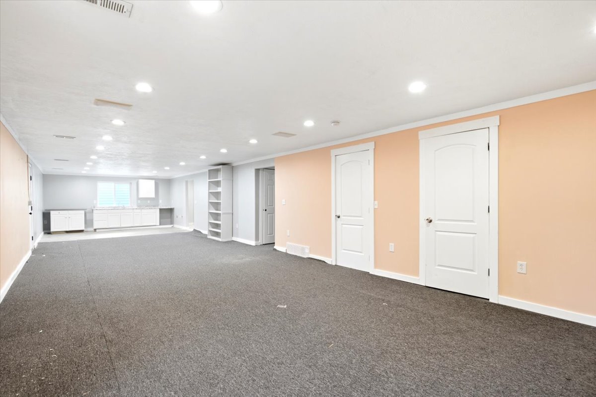 Spacious lower-level room featuring recessed lighting, a built-in shelving unit, and multiple white paneled doors