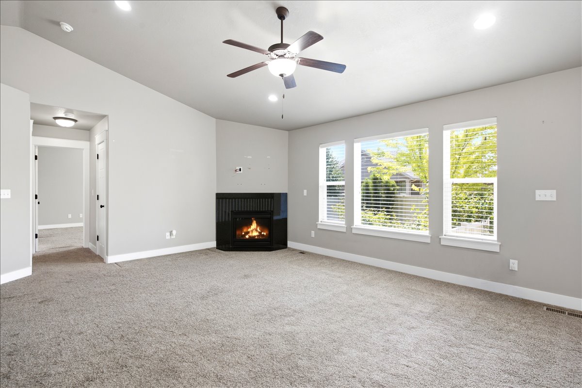 Spacious room featuring a corner fireplace with a dark mantel, multiple windows with blinds, recessed lighting, and a ceiling fan