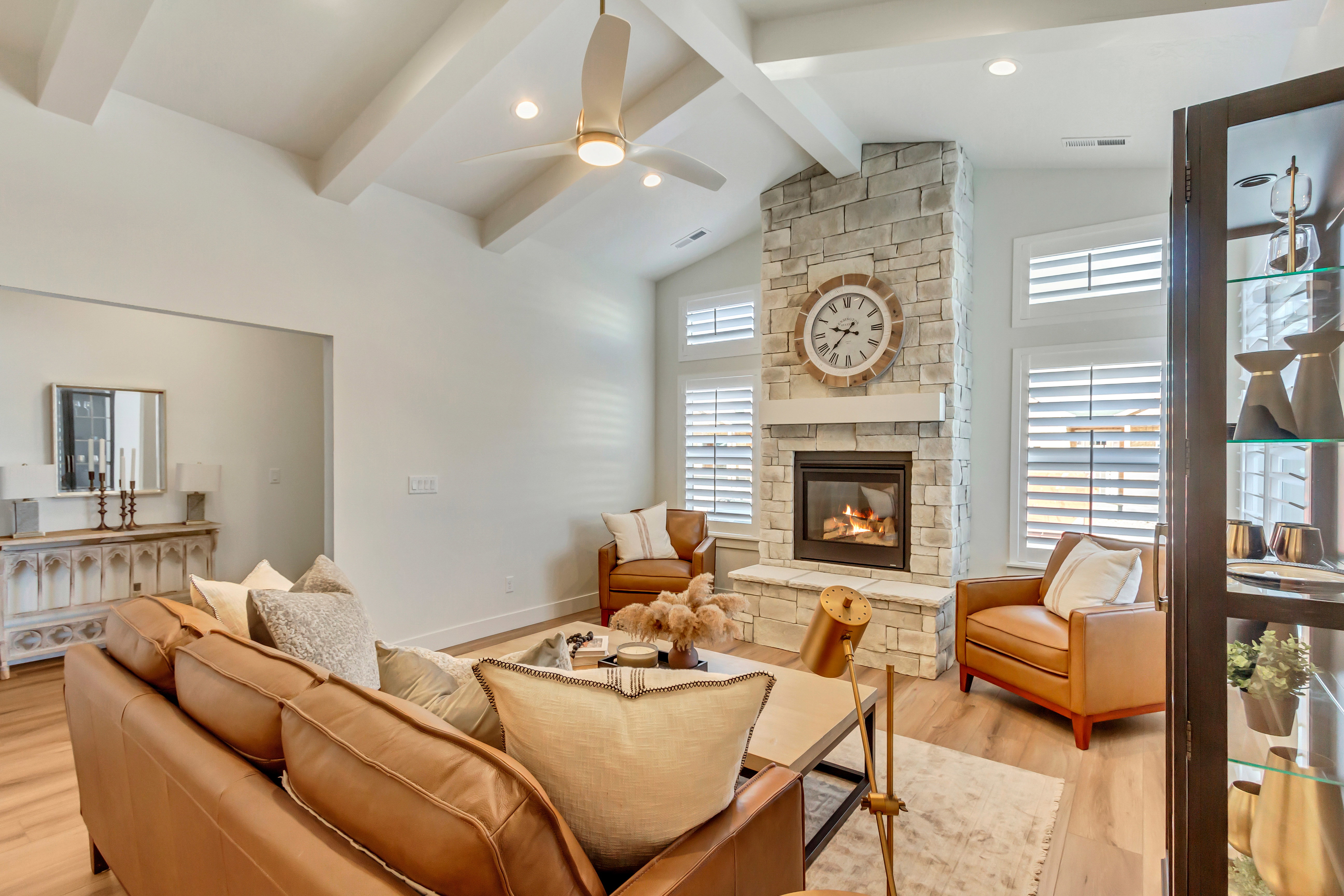 Living area featuring a stone fireplace, vaulted ceiling with exposed beams, wood-finish flooring, and white plantation shutters