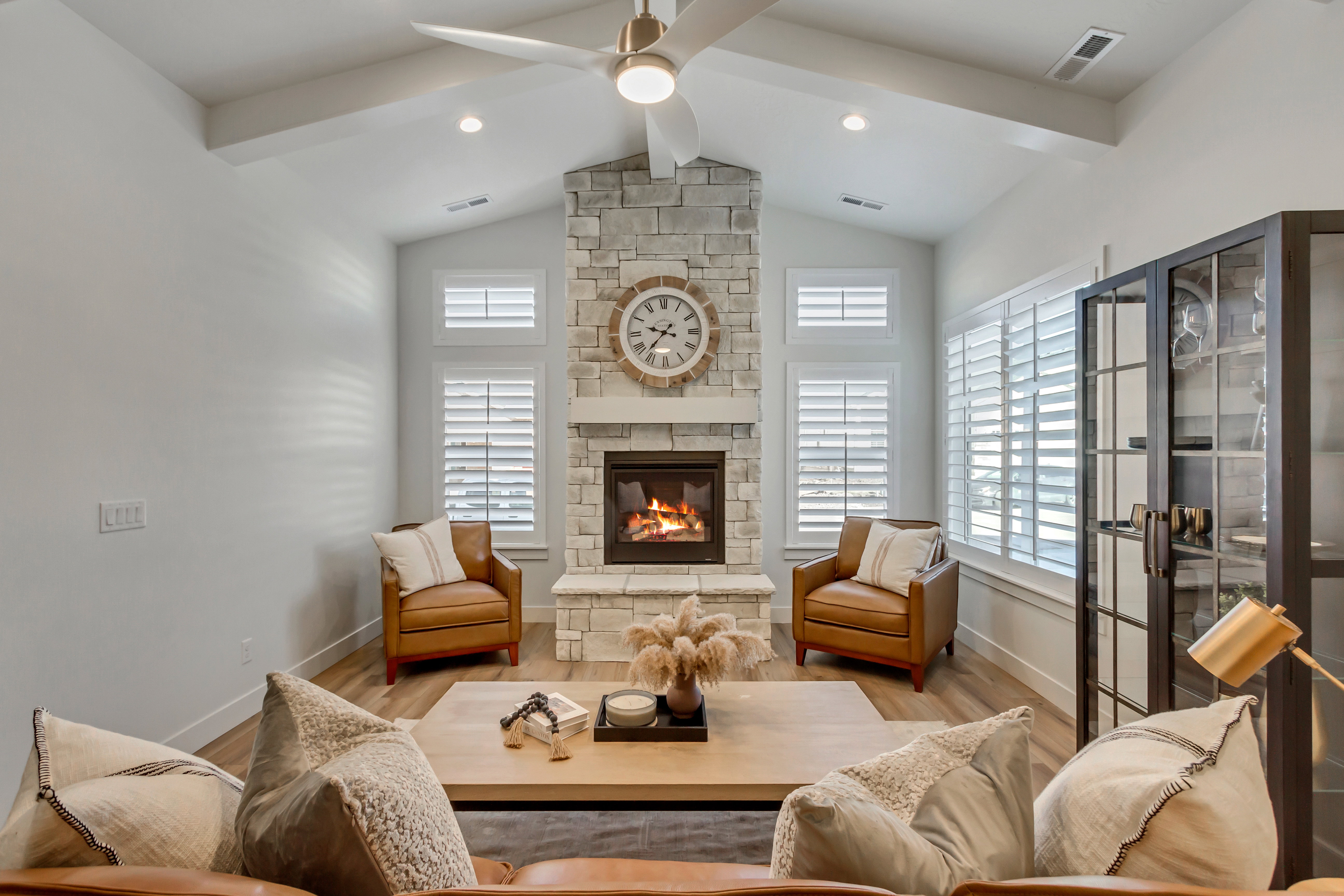 Living area featuring a stone-clad fireplace with a hearth and mantle, vaulted ceilings with exposed beams, wood-finish flooring, and white plantation shutters