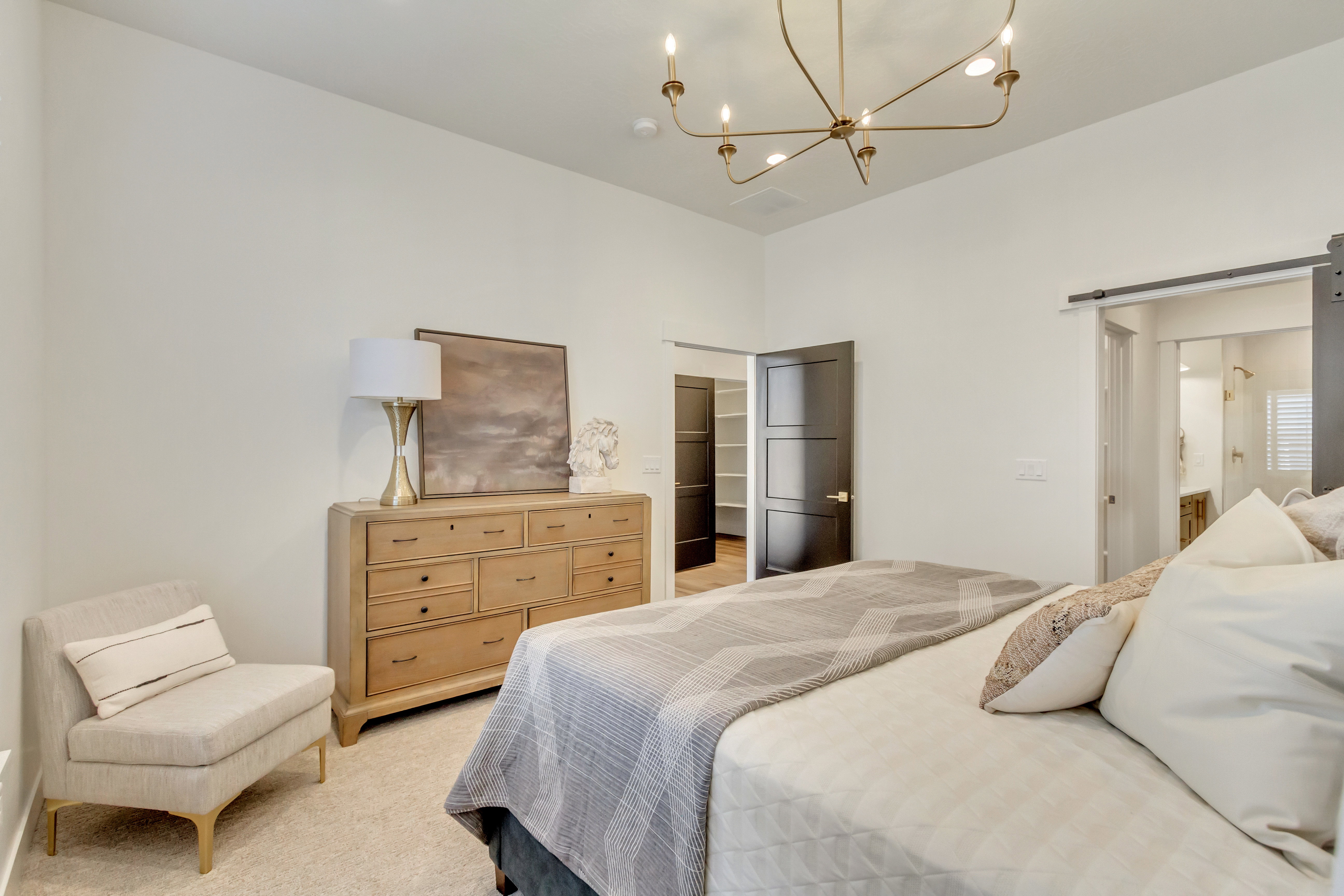 Modern brass chandelier illuminating a spacious room with light-toned walls and carpet flooring