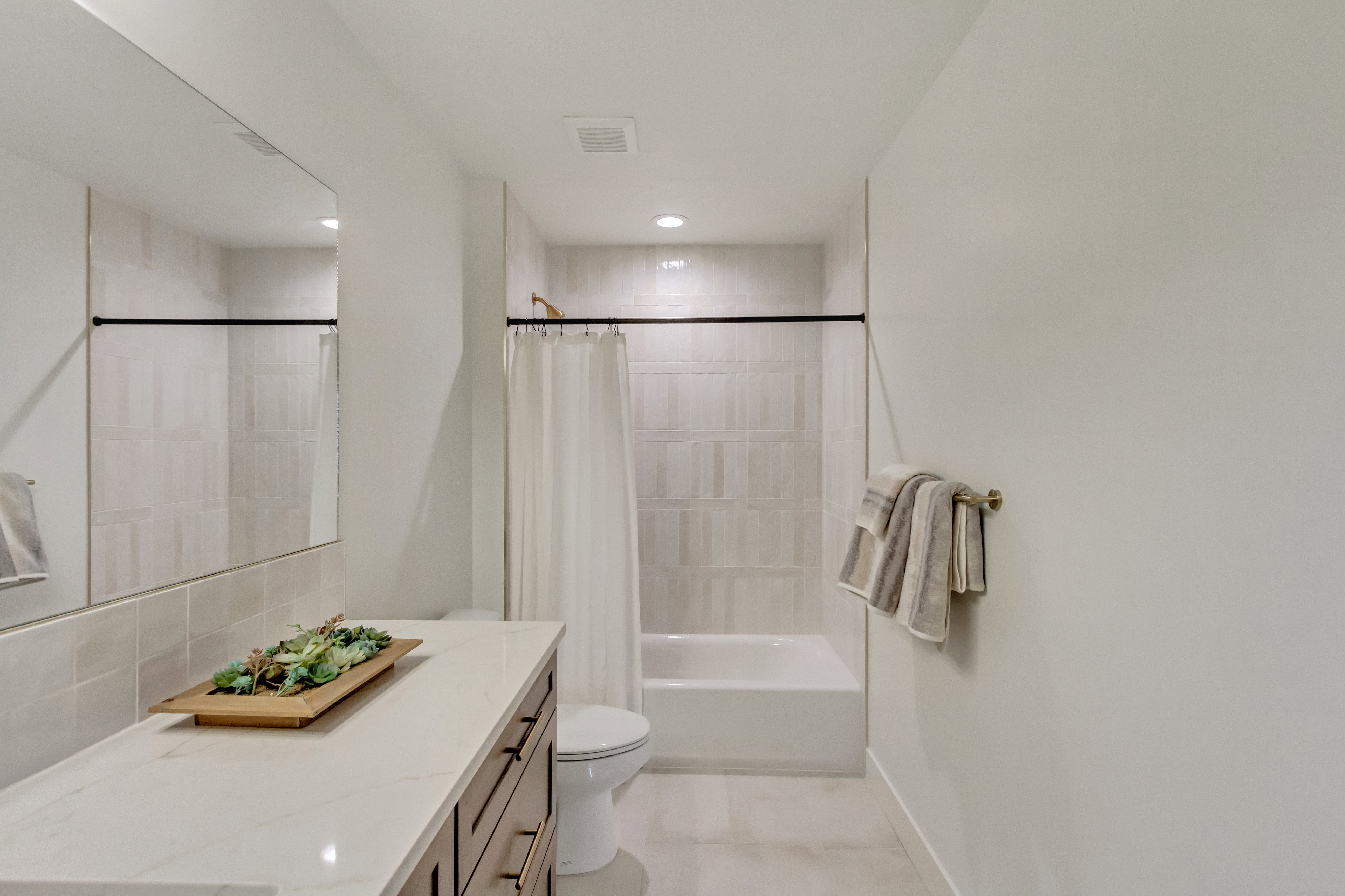Bathroom featuring a white bathtub with tile surround, a dark wood-finish vanity with a light-toned countertop, and a large wall-mounted mirror