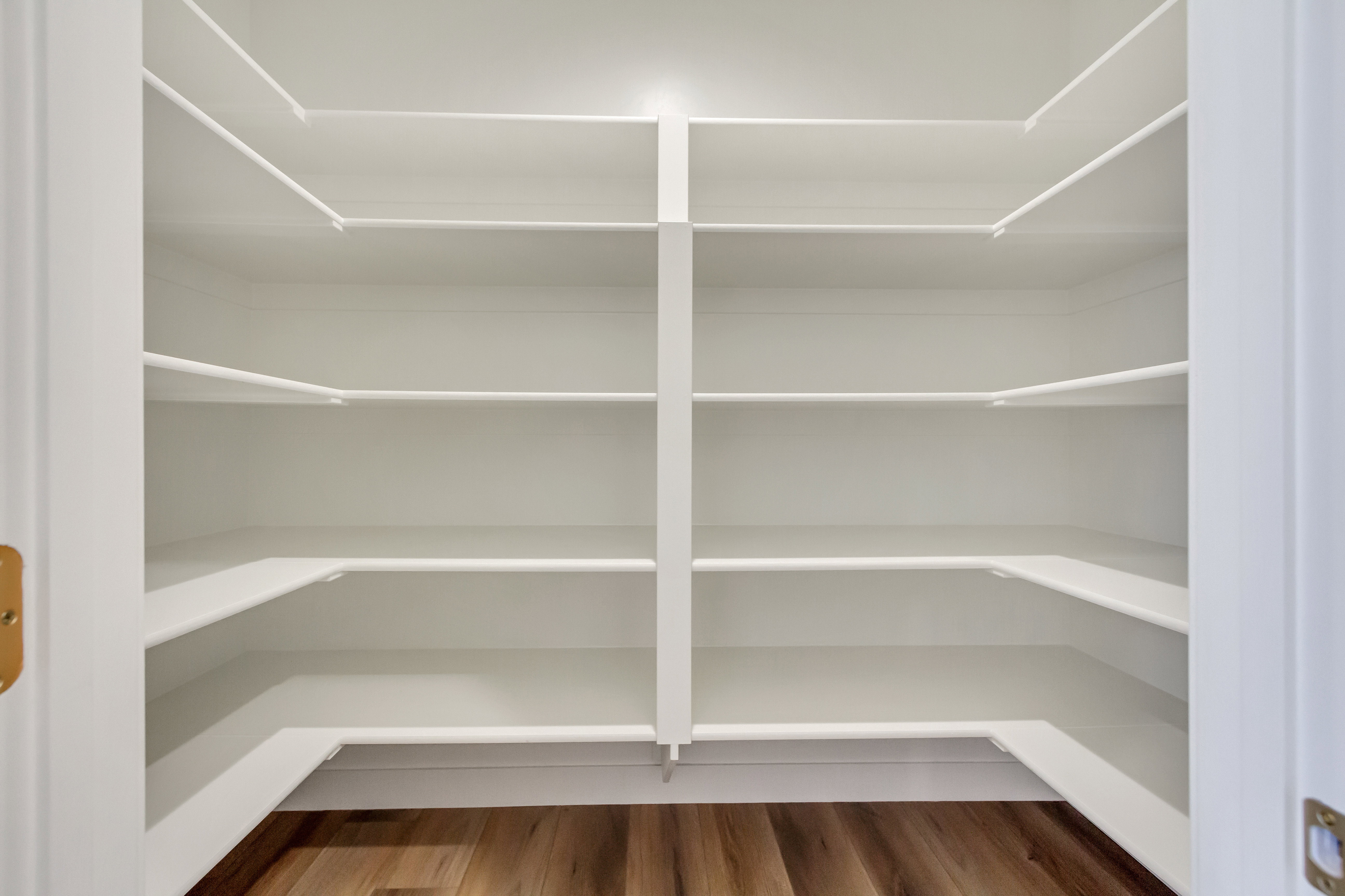 Spacious walk-in pantry featuring white shelving, multiple storage levels, and wood-finish flooring