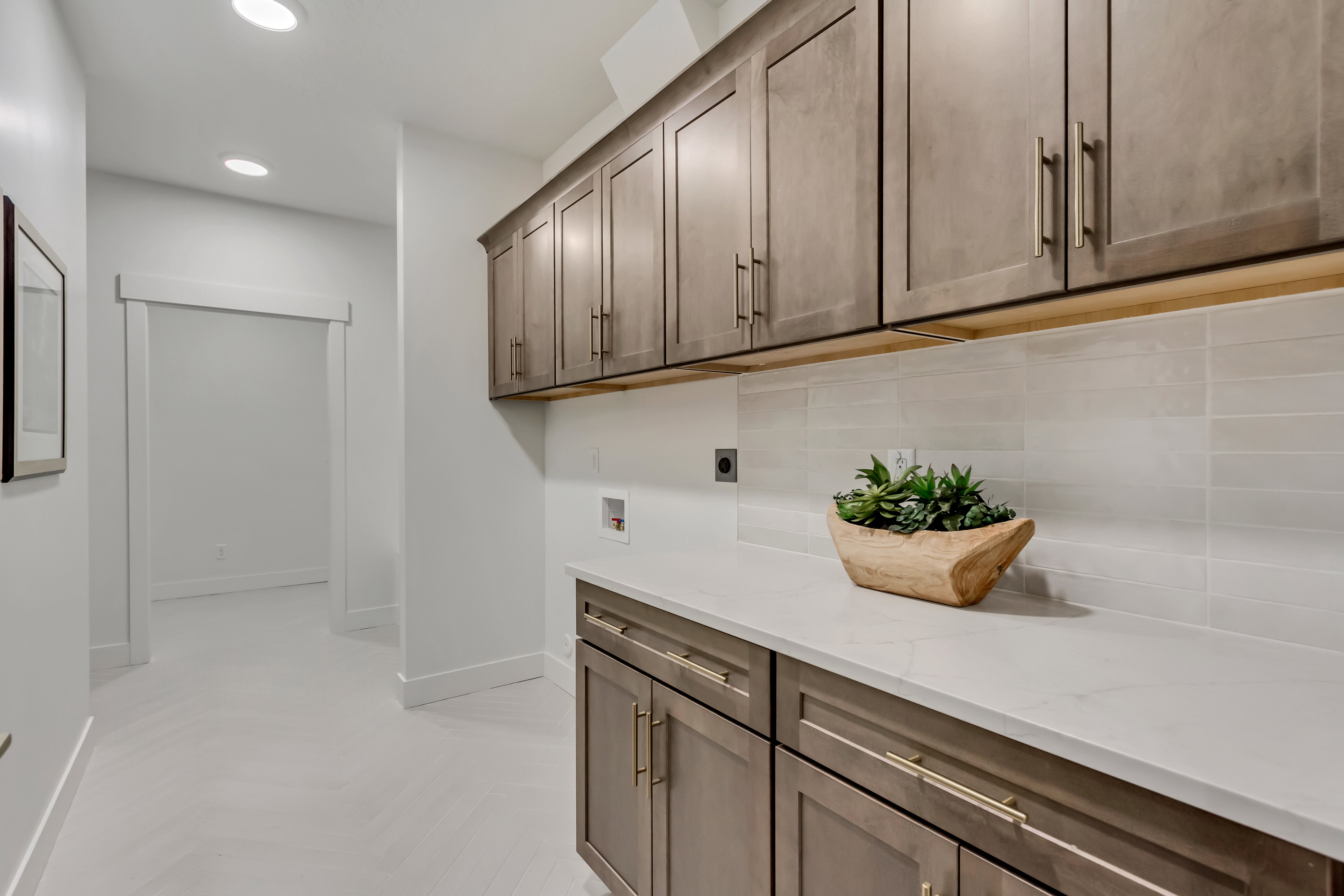 Laundry area featuring extensive upper and lower cabinetry with gold-tone hardware, a light-toned countertop, and a tiled backsplash