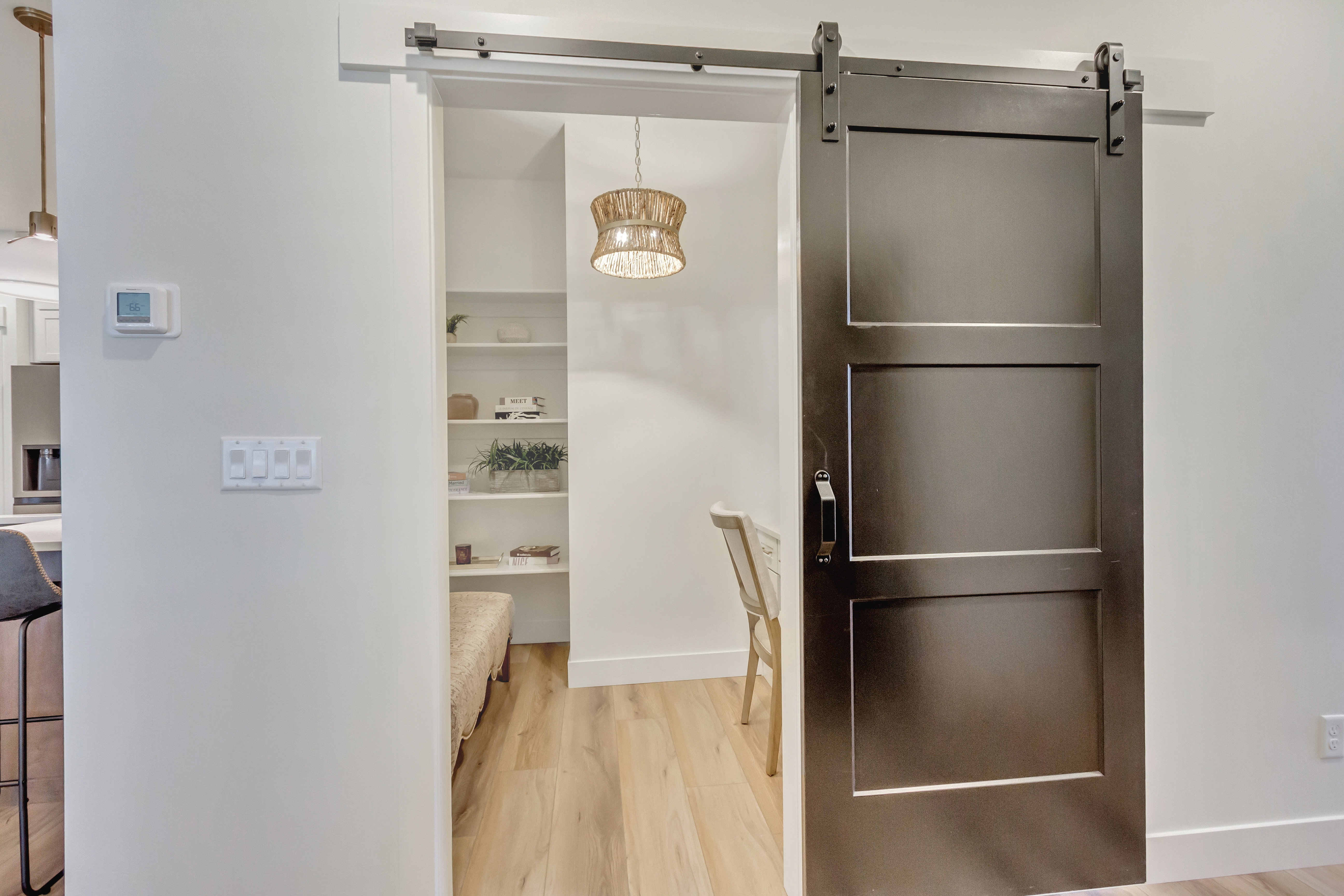 Dark-paneled barn door with a matte black track system, opening to an interior space with light wood-finish flooring