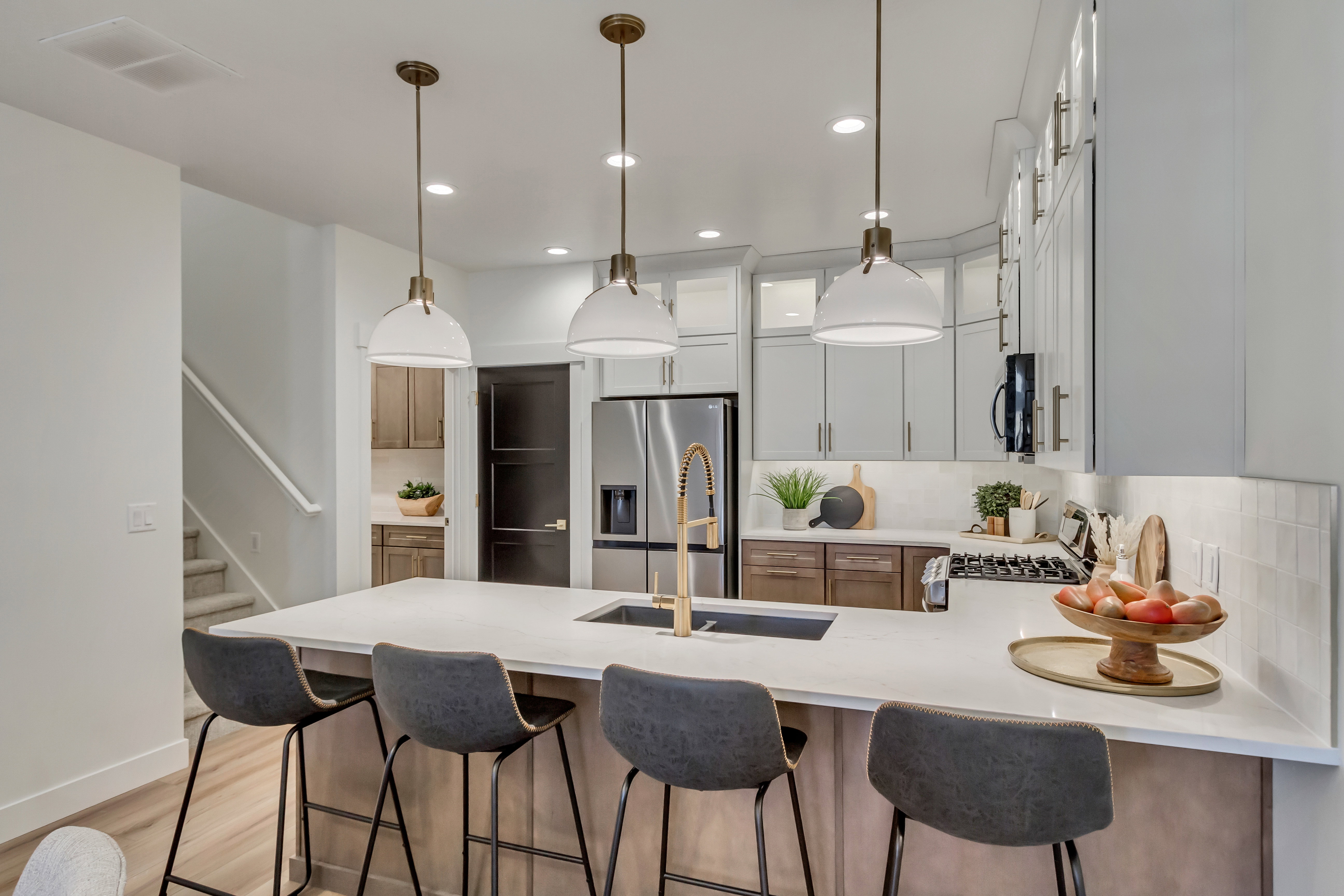 Modern kitchen featuring a large island with seating, stainless steel appliances, white subway tile backsplash, and two-tone cabinetry with under-cabinet lighting