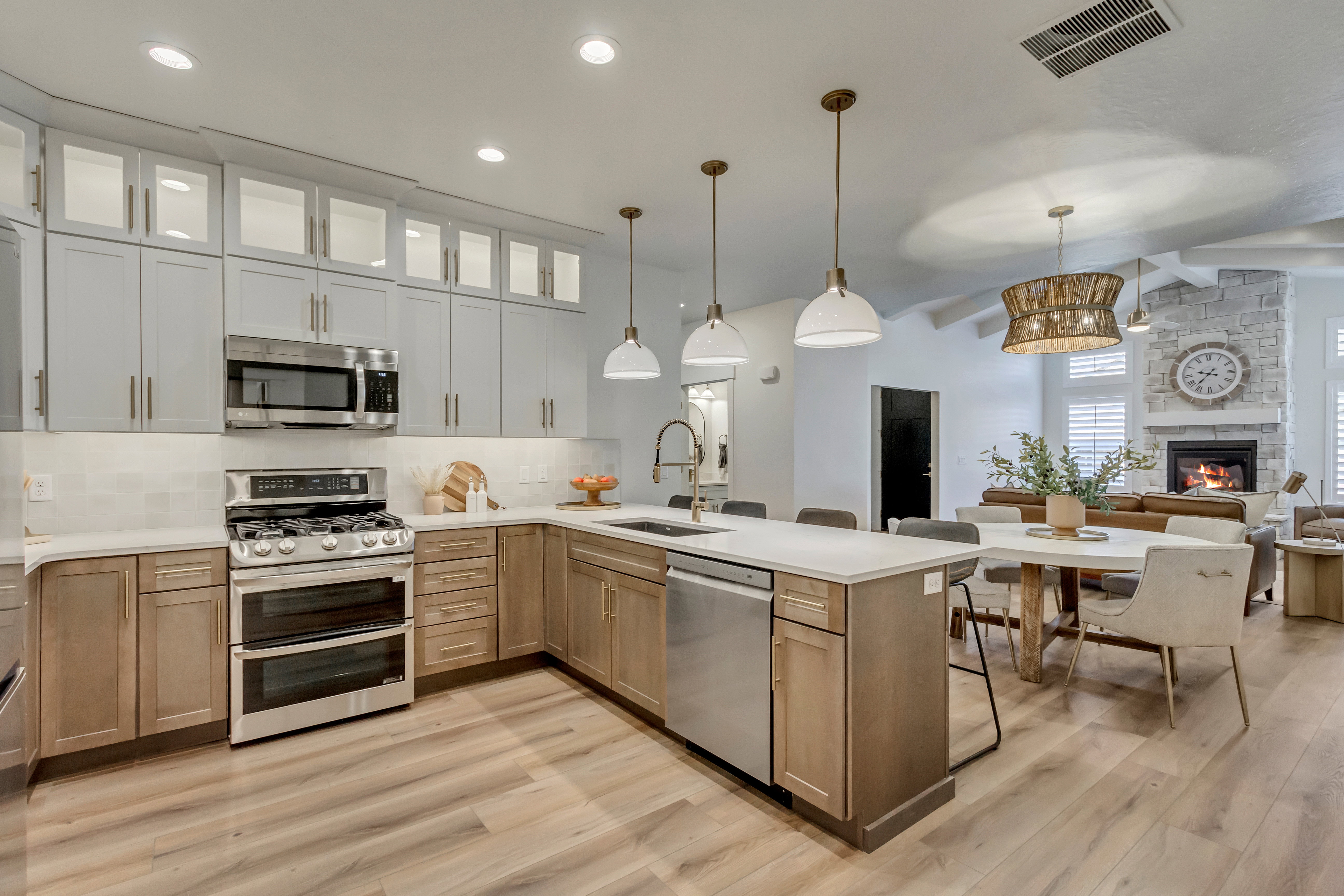 Open-concept kitchen featuring two-tone cabinetry, stainless steel appliances, a white tile backsplash, and light wood-finish flooring