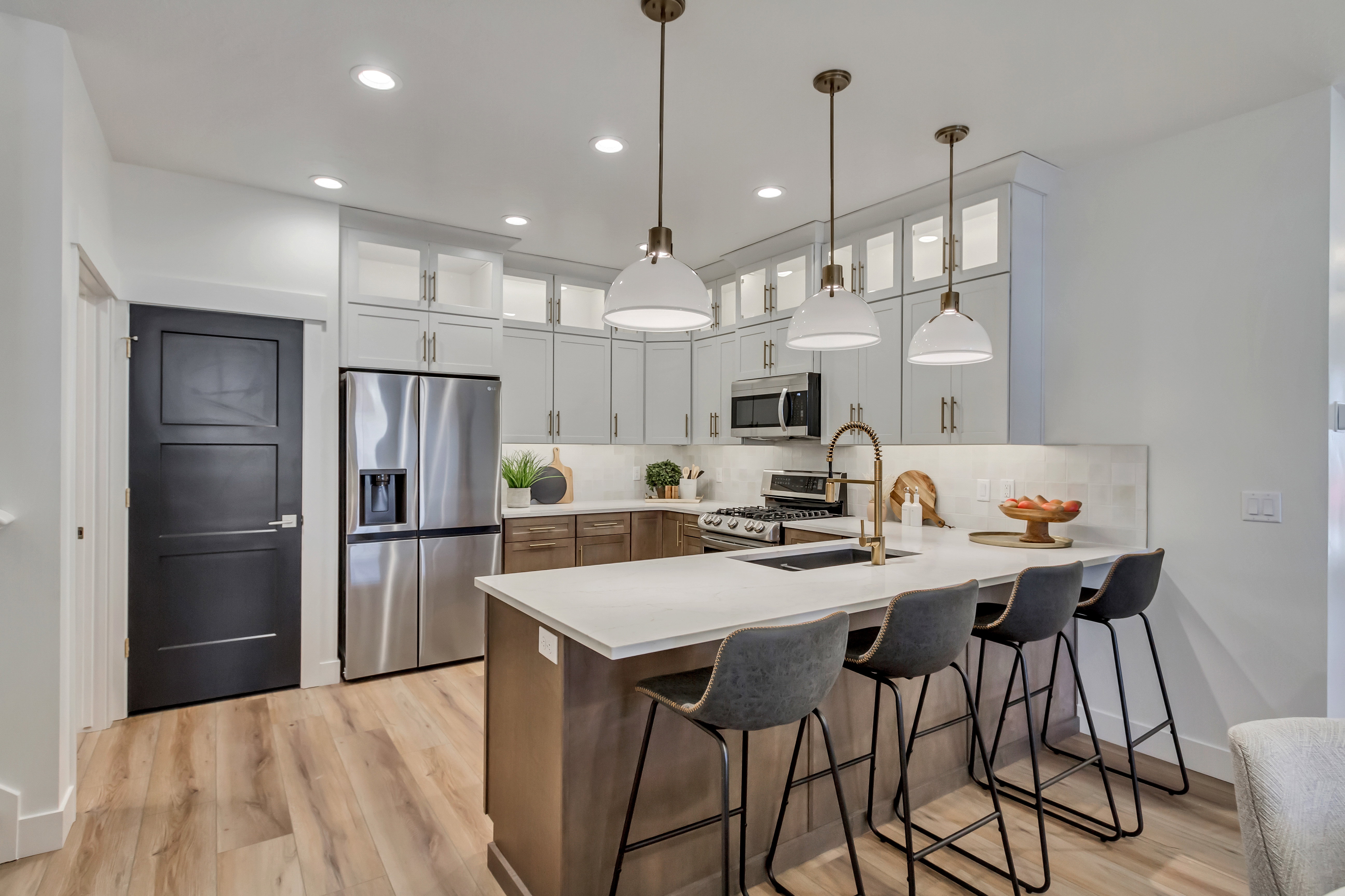 Kitchen featuring a large central island with seating, stainless steel appliances, a tile backsplash, wood-finish flooring, and pendant lighting