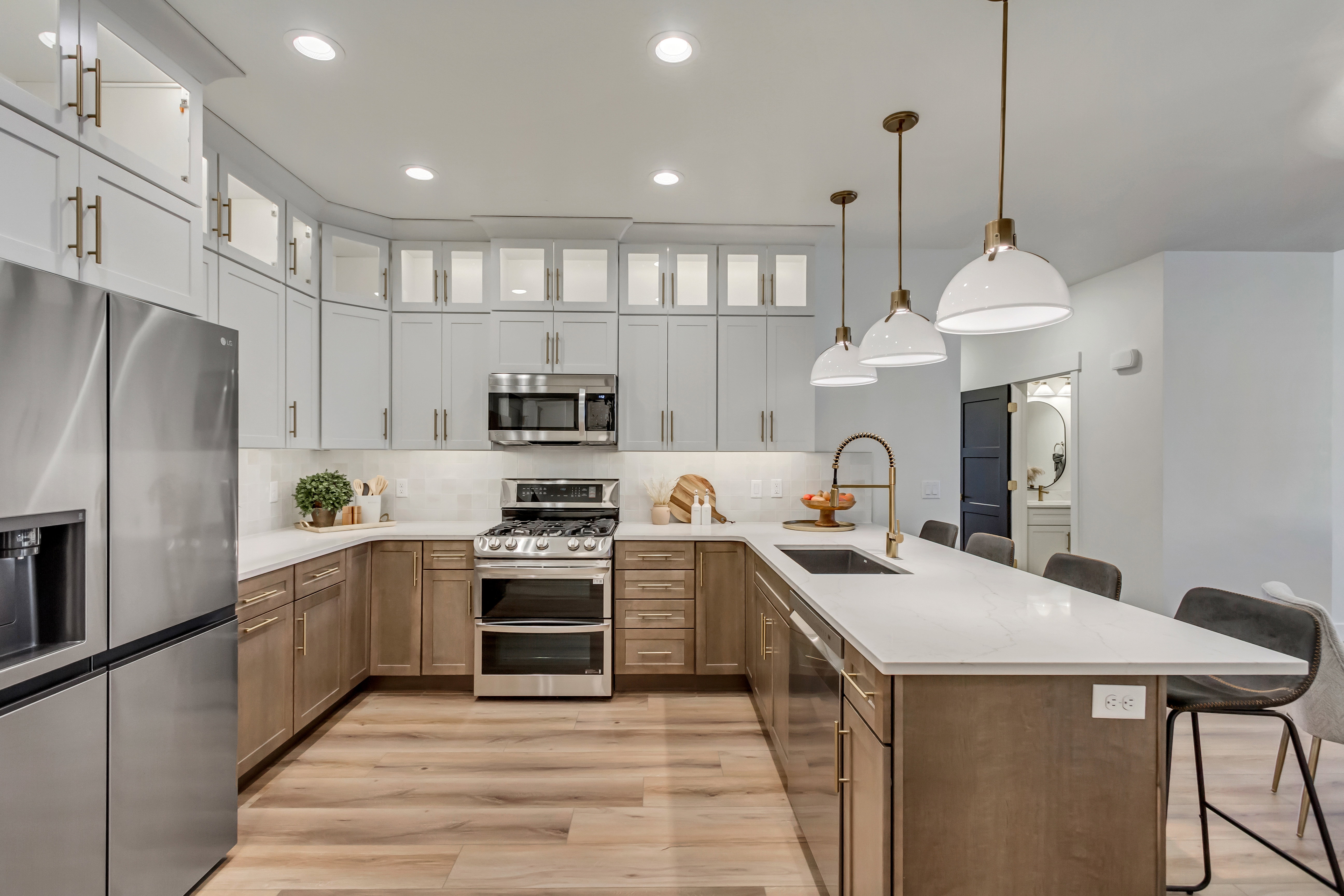 Contemporary kitchen featuring two-tone cabinetry, stainless steel appliances, a large island with sink, pendant lighting, and wood-finish flooring