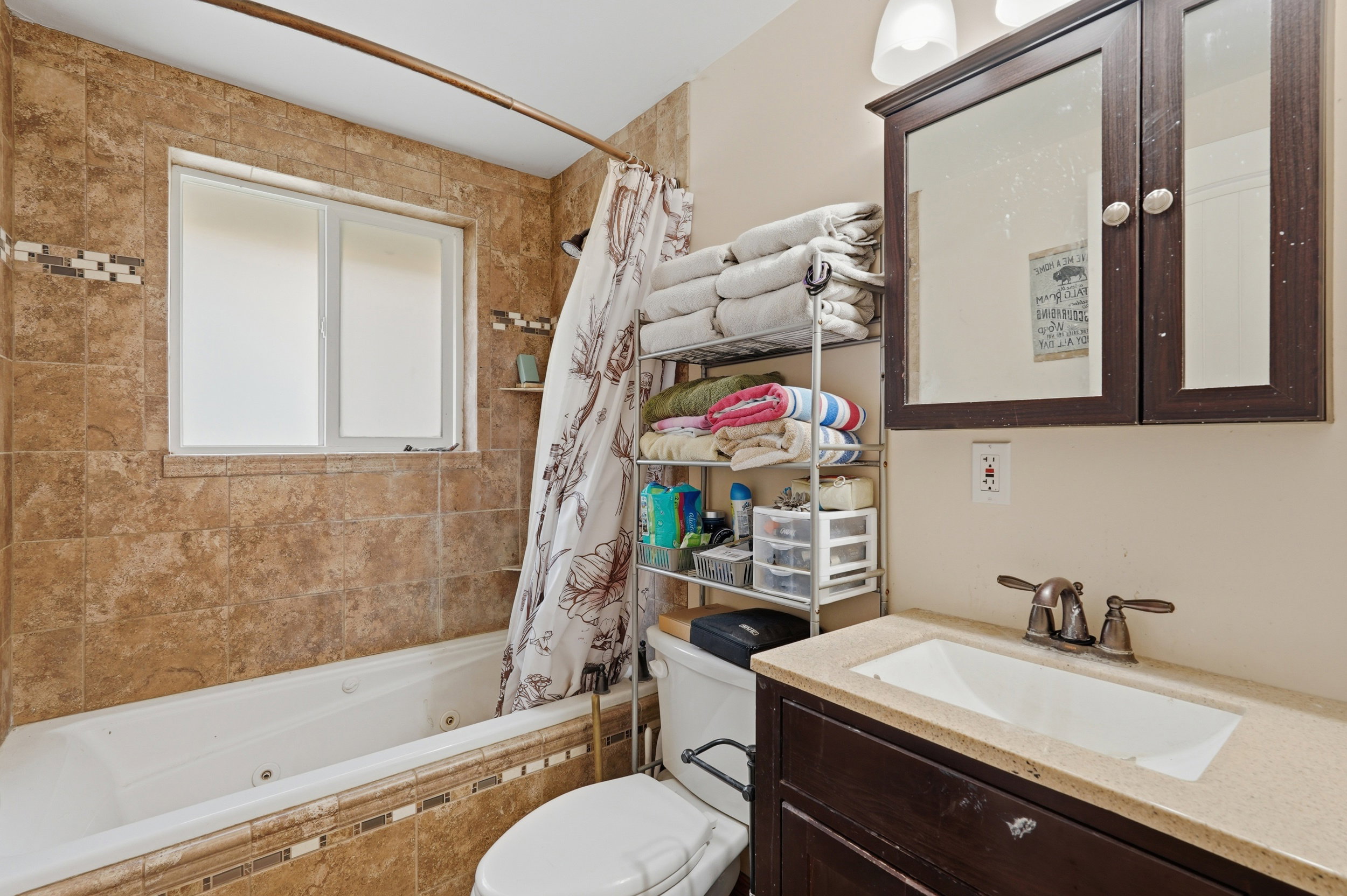 Bathroom featuring a tiled bathtub surround with an inset window, a dark wood-finish vanity with an integrated sink, bronze-finish faucet, and a wall-mounted medicine cabinet with a mirror
