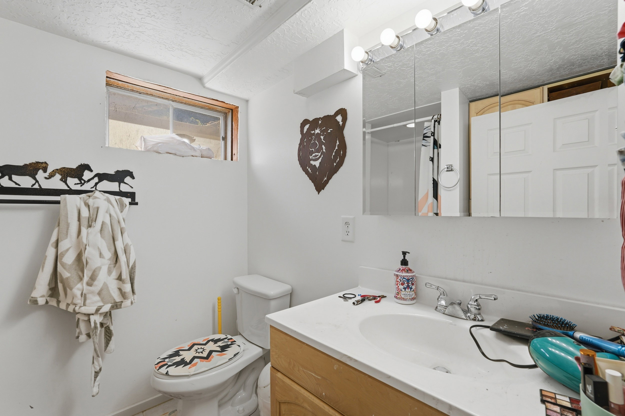 Bathroom featuring a single vanity with light-colored countertop, wall-mounted mirror with integrated lighting, and a window for natural illumination