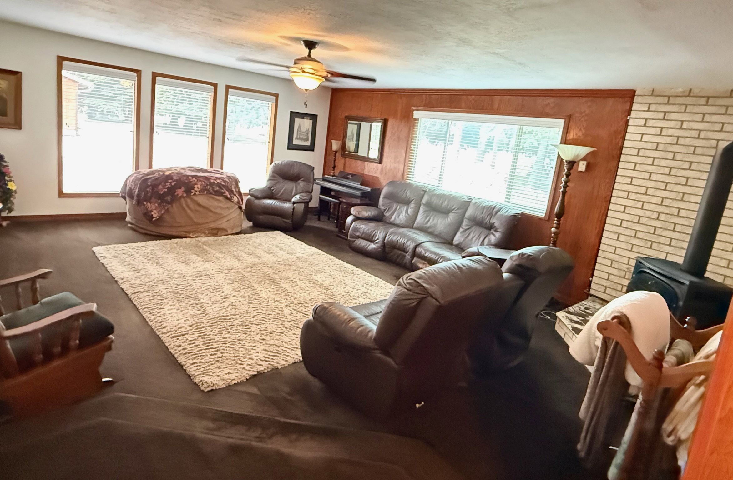 Spacious interior featuring a wood-burning stove with a brick surround, wood paneling, and multiple windows