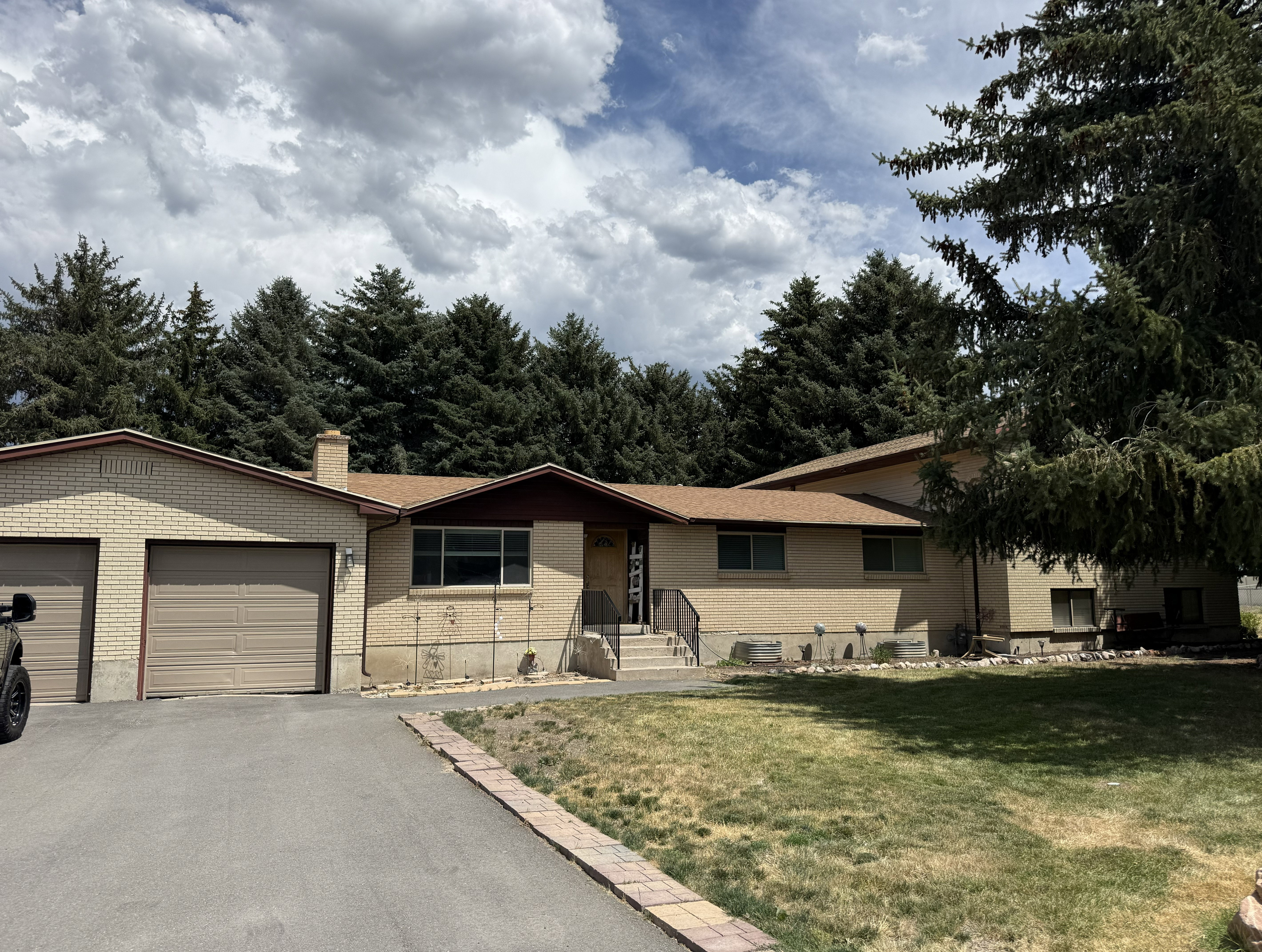 Ranch-style residence featuring brick siding, a two-car attached garage, and mature evergreen landscaping