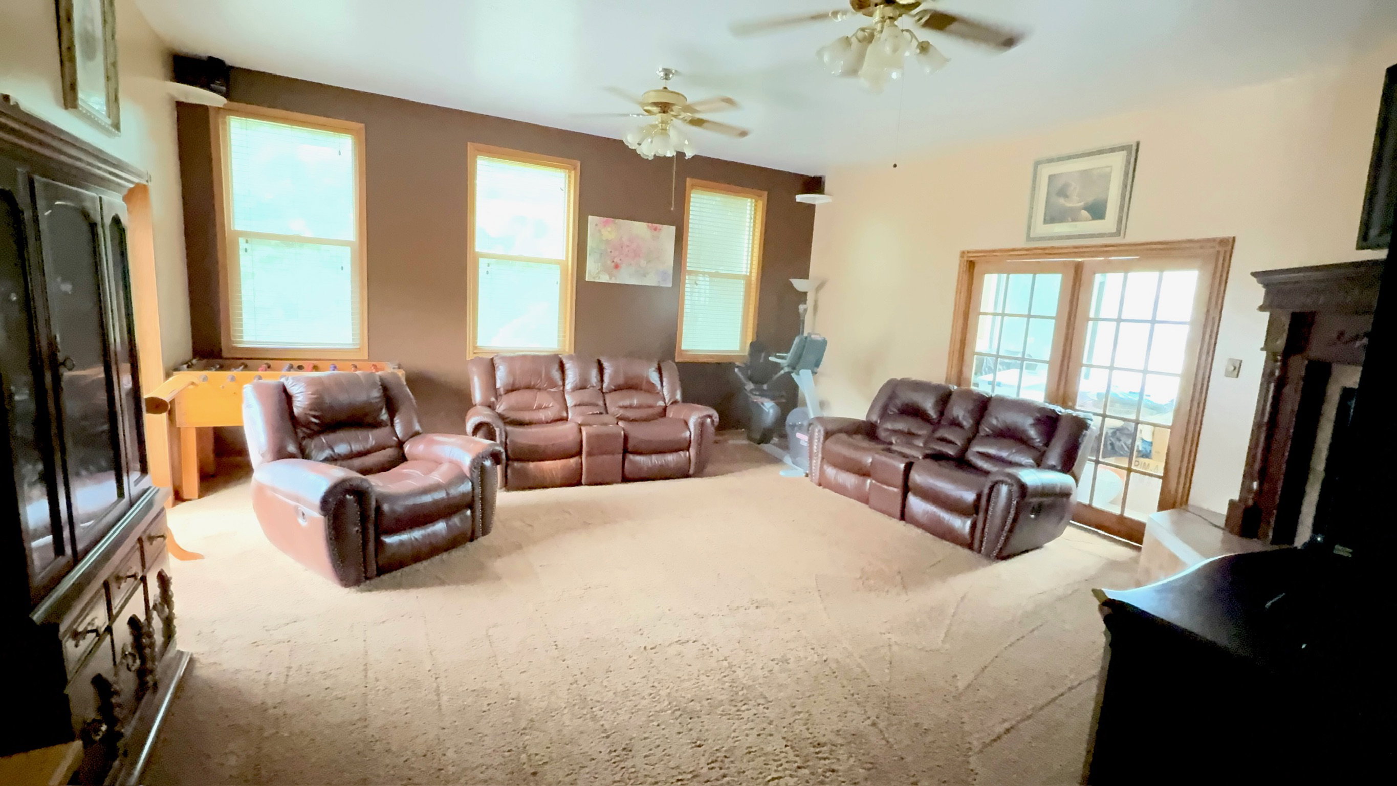 Spacious living area featuring carpet flooring, multiple windows, a stone fireplace, and French doors