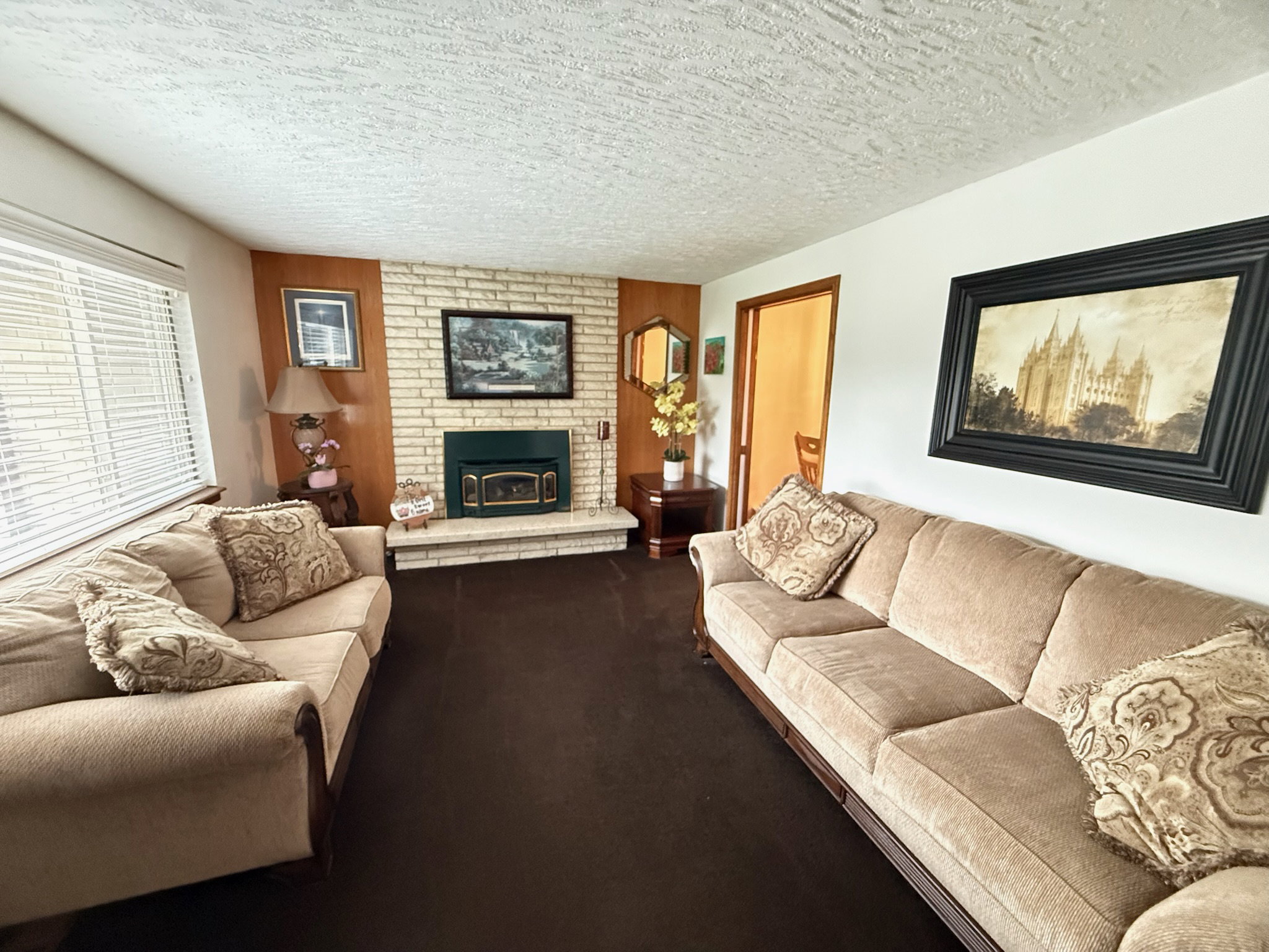 Living area featuring a brick-faced fireplace with a green insert, wood paneling accents, and window blinds