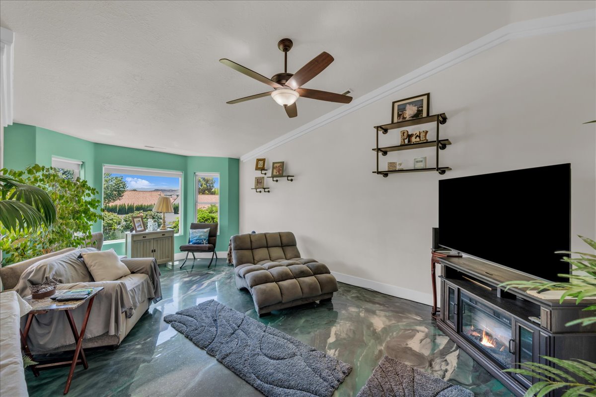 Spacious living area featuring polished green flooring, a ceiling fan, and crown molding