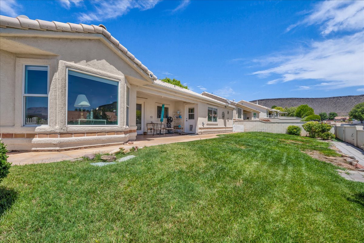 Exterior featuring an expansive window, covered patio, stucco siding, and a terraced backyard with a rock backdrop