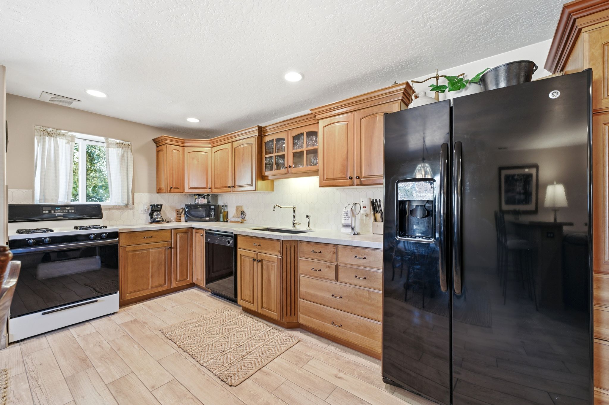 Kitchen featuring light wood-finish cabinetry, white countertops, and a black appliance suite including a side-by-side refrigerator