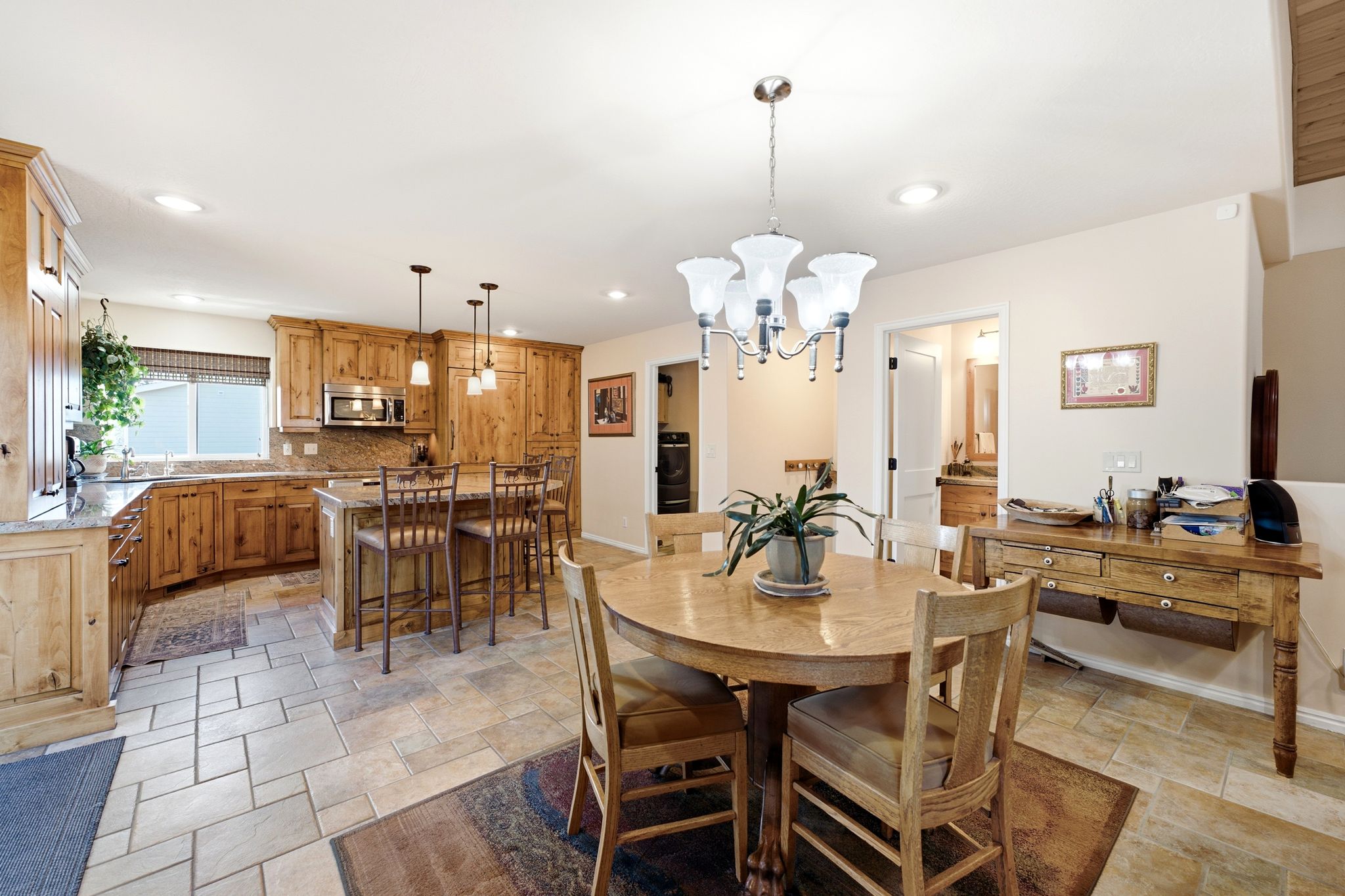 Open-concept kitchen and dining area featuring stone tile flooring, natural wood cabinetry, a central island with bar seating, and recessed lighting
